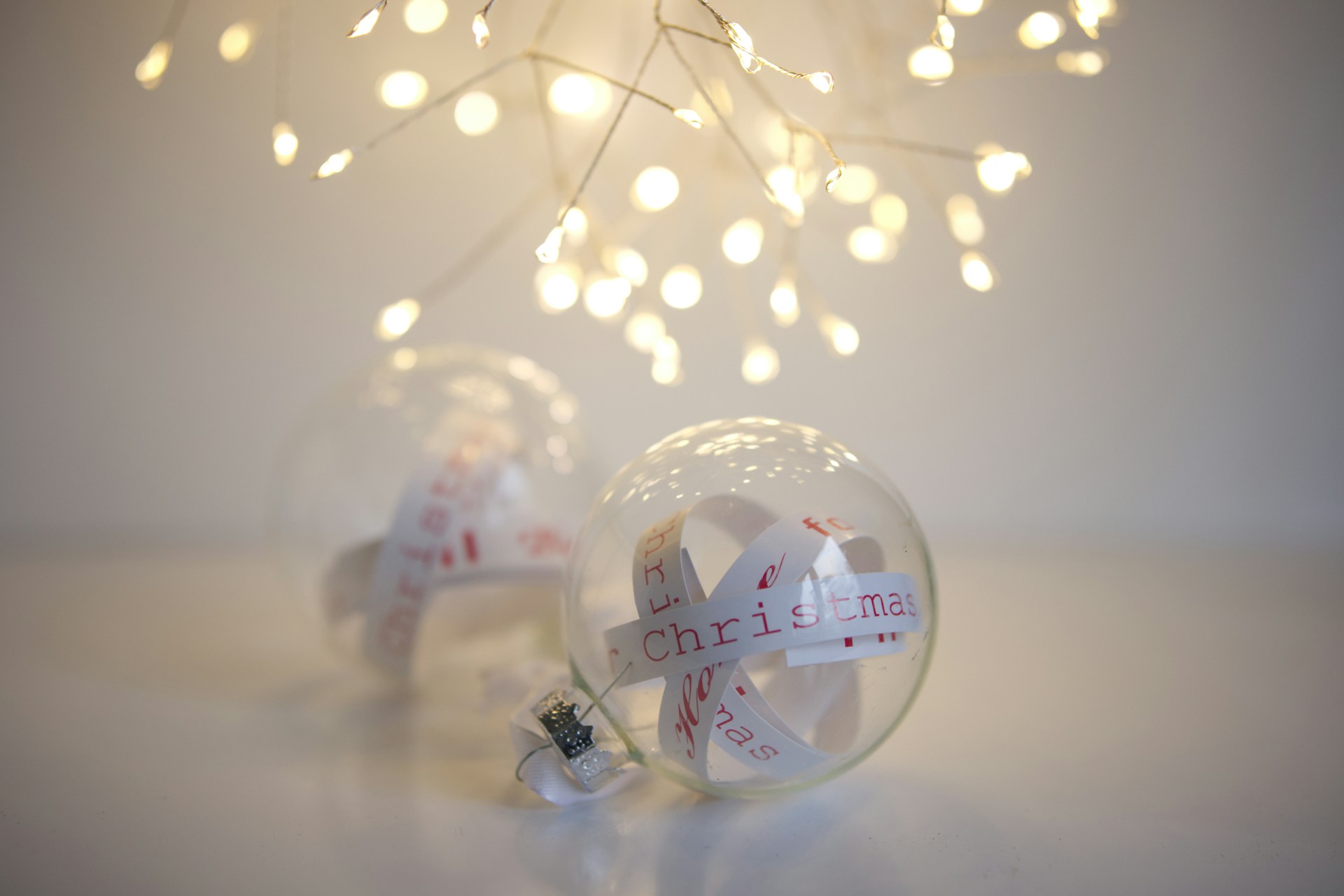 Clear glass ornaments with curled paper strips with handwritten Christmas words under soft lights