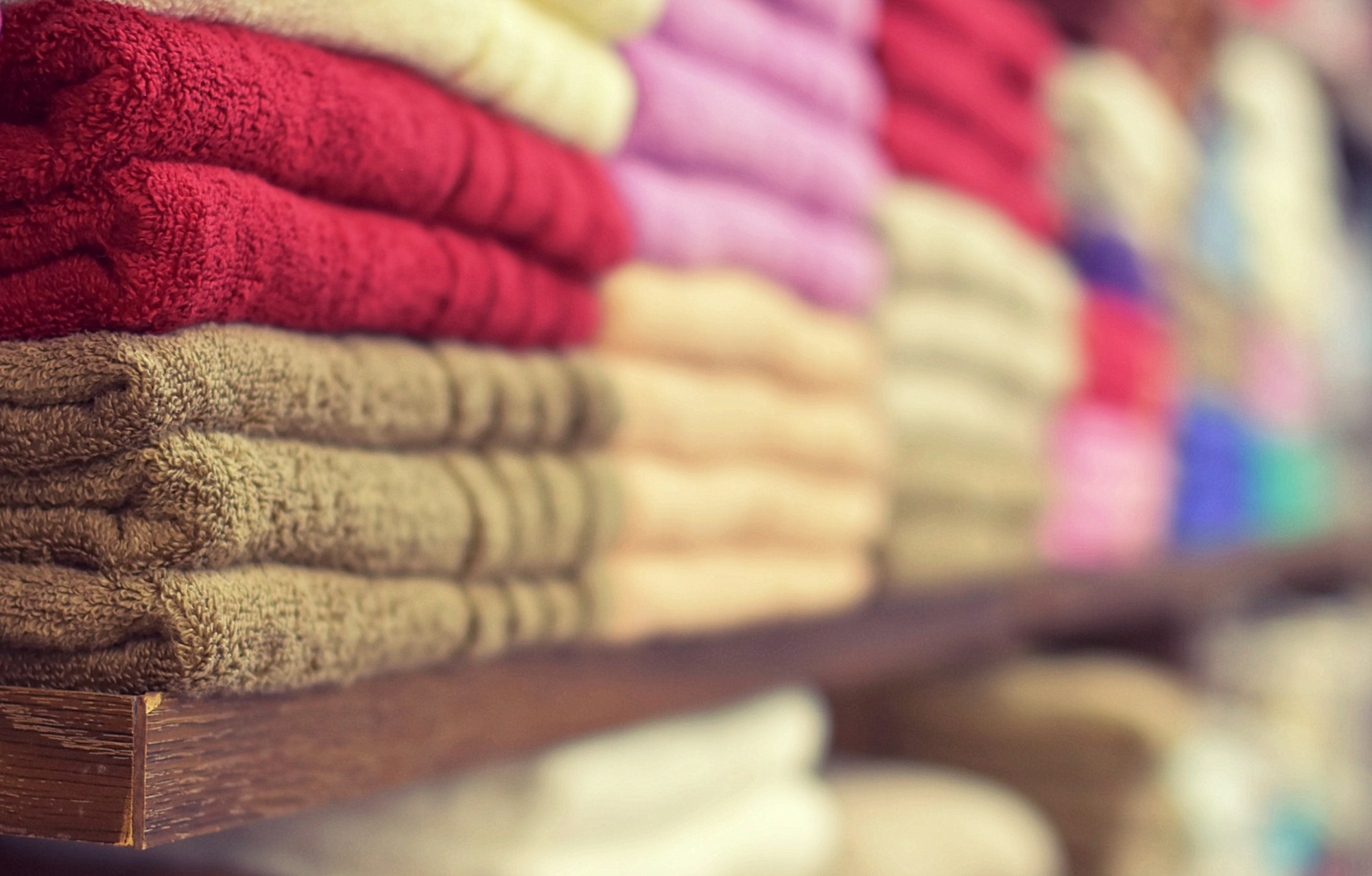Old towel upcycles start here: stacks of colorful folded towels on a wooden shelf
