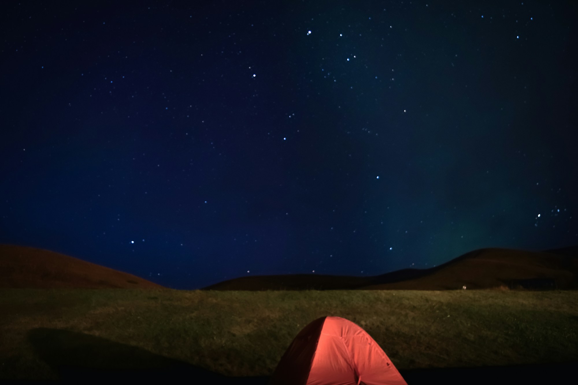 Red tent glowing under a starry night sky