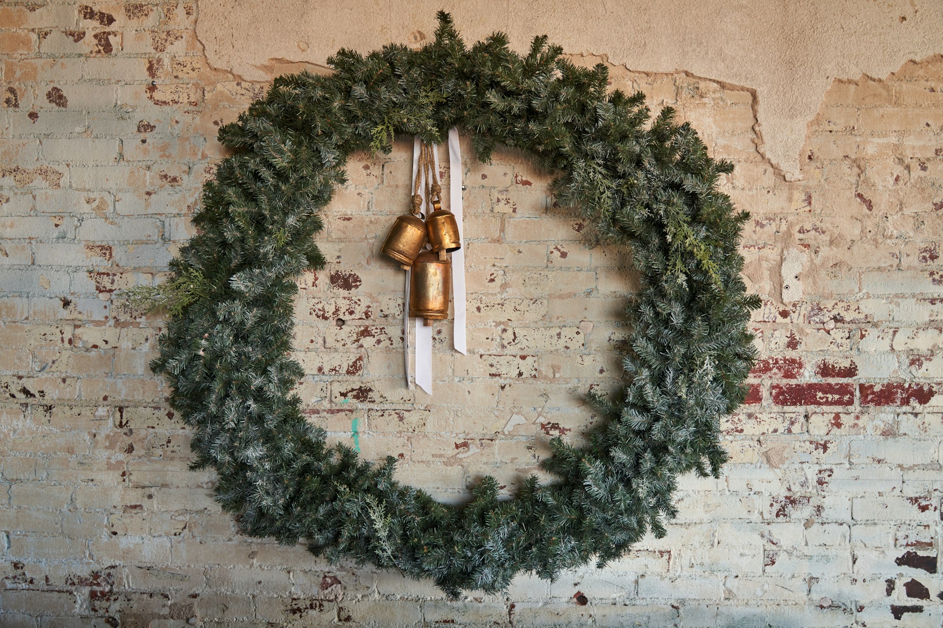 Green wreath with brass bells hanging in the center on a white brick wall