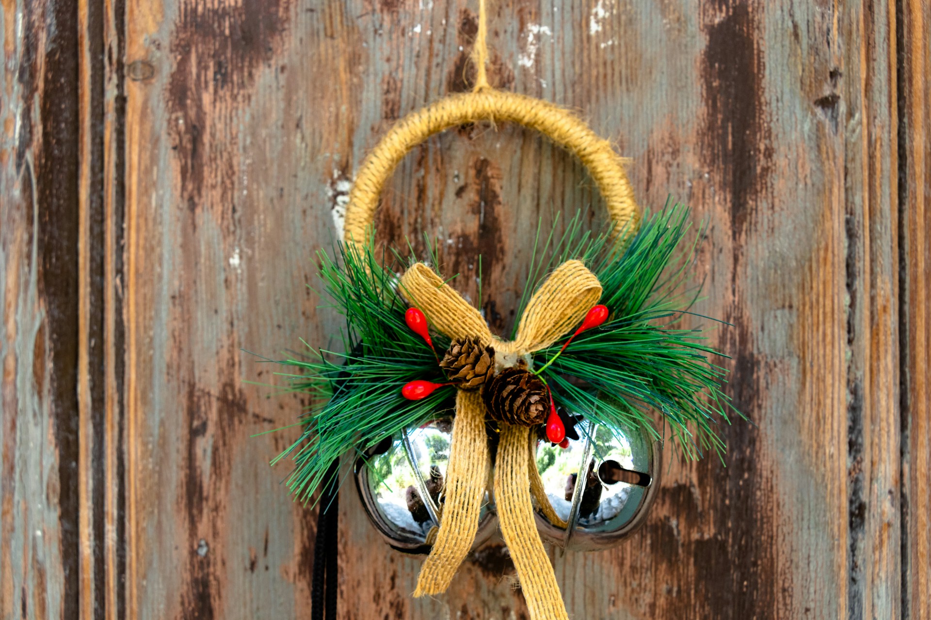 Silver bells with a gold bow and pine sprigs hanging on a rustic wooden door