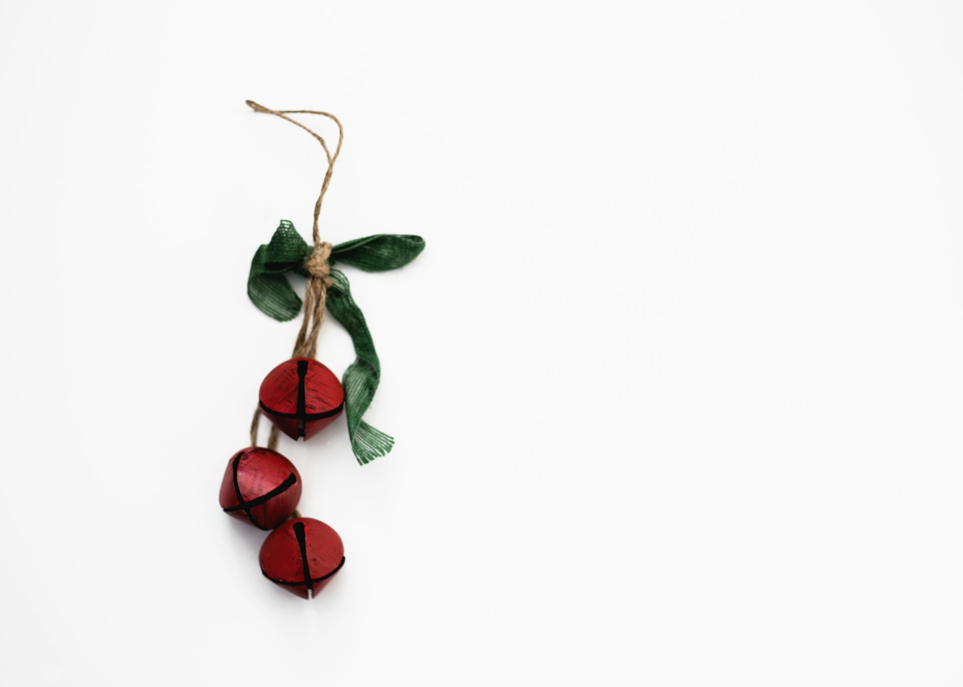 Red jingle bells tied with a green ribbon on a white background