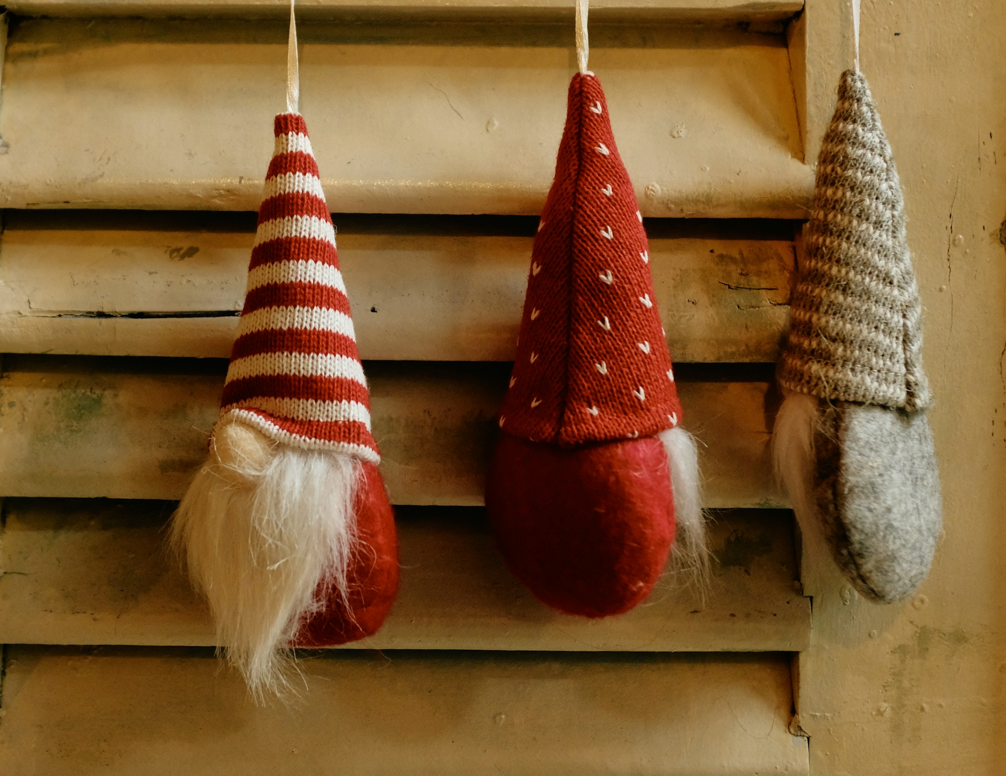 Three fabric gnomes with striped hats hanging on a wooden shutter