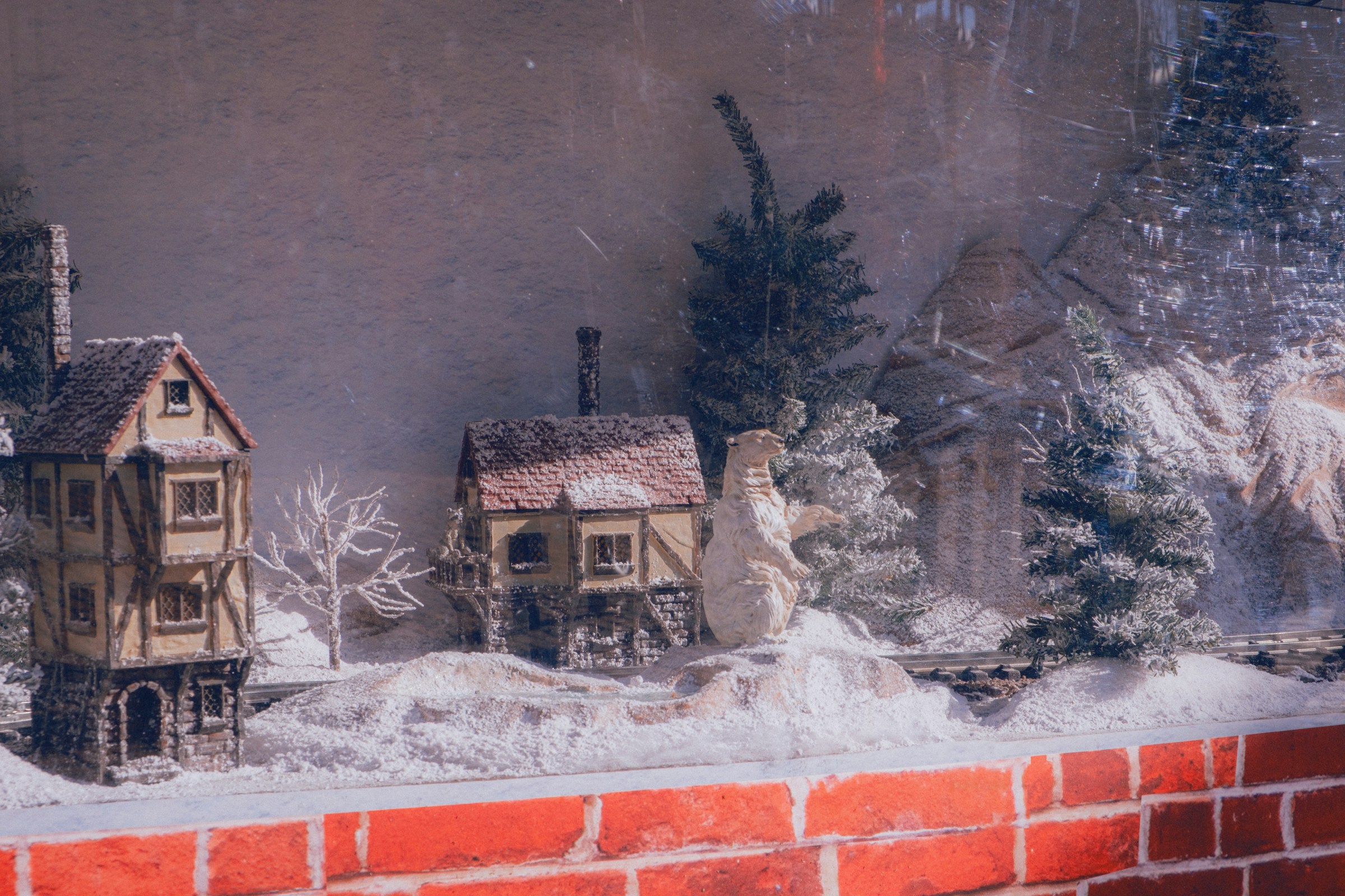 Miniature winter village houses and frosted trees on a thick bed of snow along a brick ledge