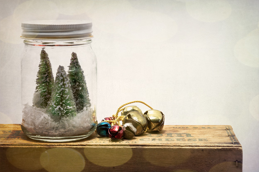Dollar Store Christmas Decor jar holding small bottle brush trees and faux snow beside jingle bells