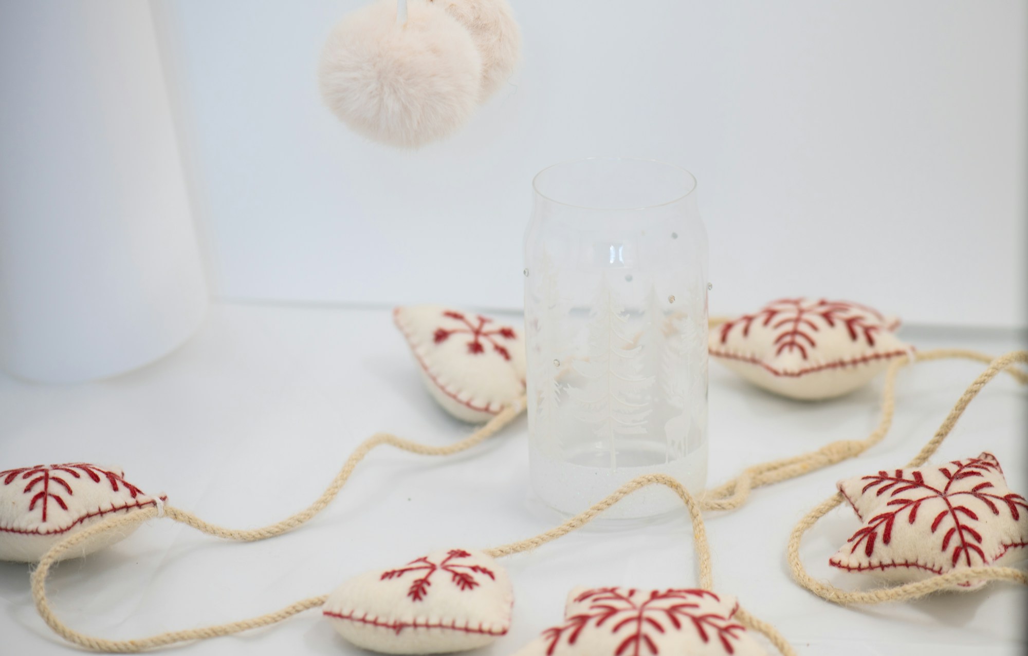 Stuffed felt ornament garland with red snowflake embroidery beside a glass tumbler