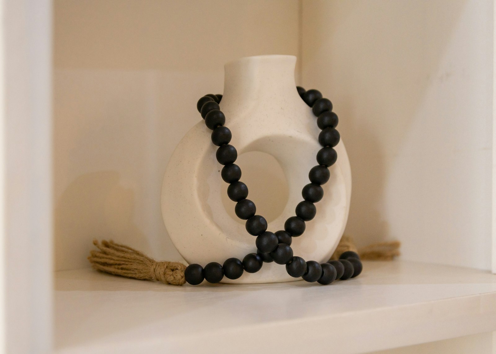 Black beaded garland draped beside a white vase on a styled shelf