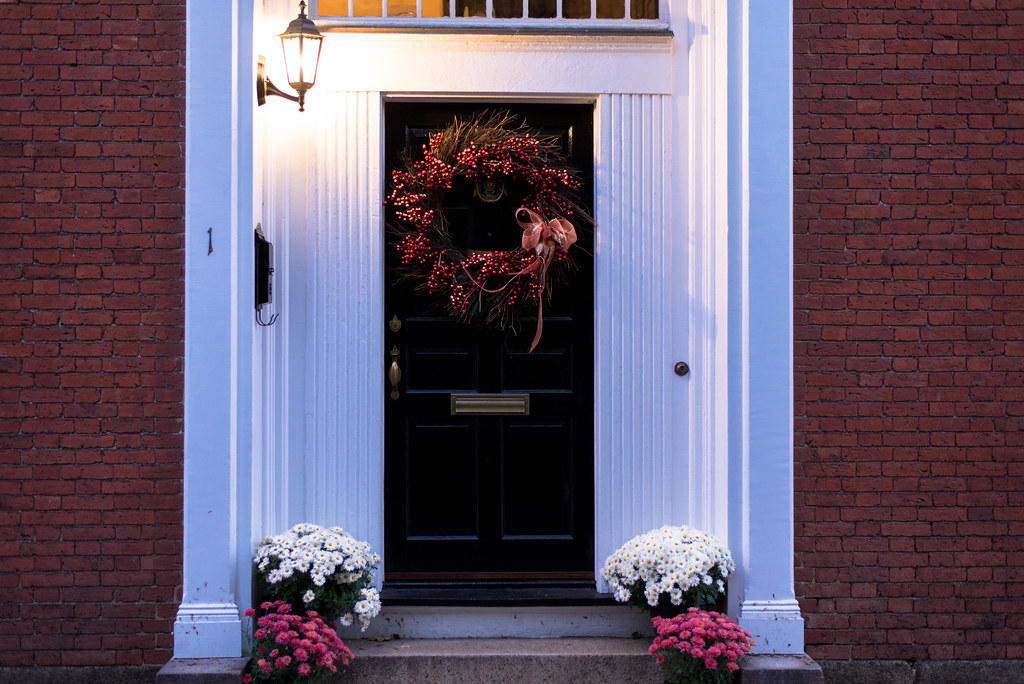 Full autumn wreath with red and gold leaves on a black front door framed by white mums