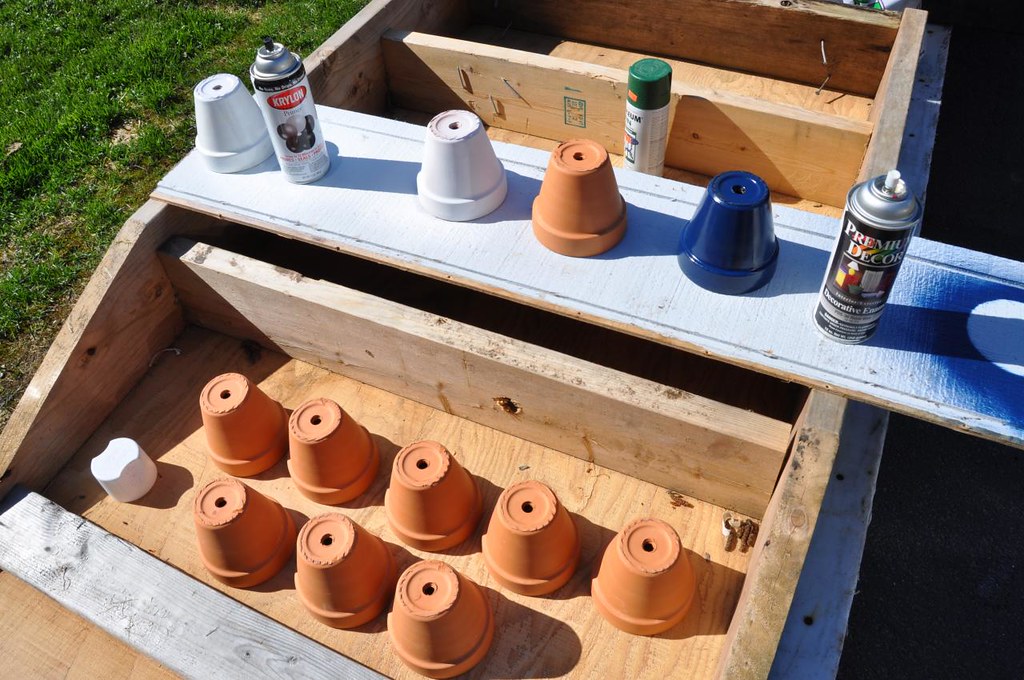 Rows of small terracotta pots on a wooden board ready for spray paint