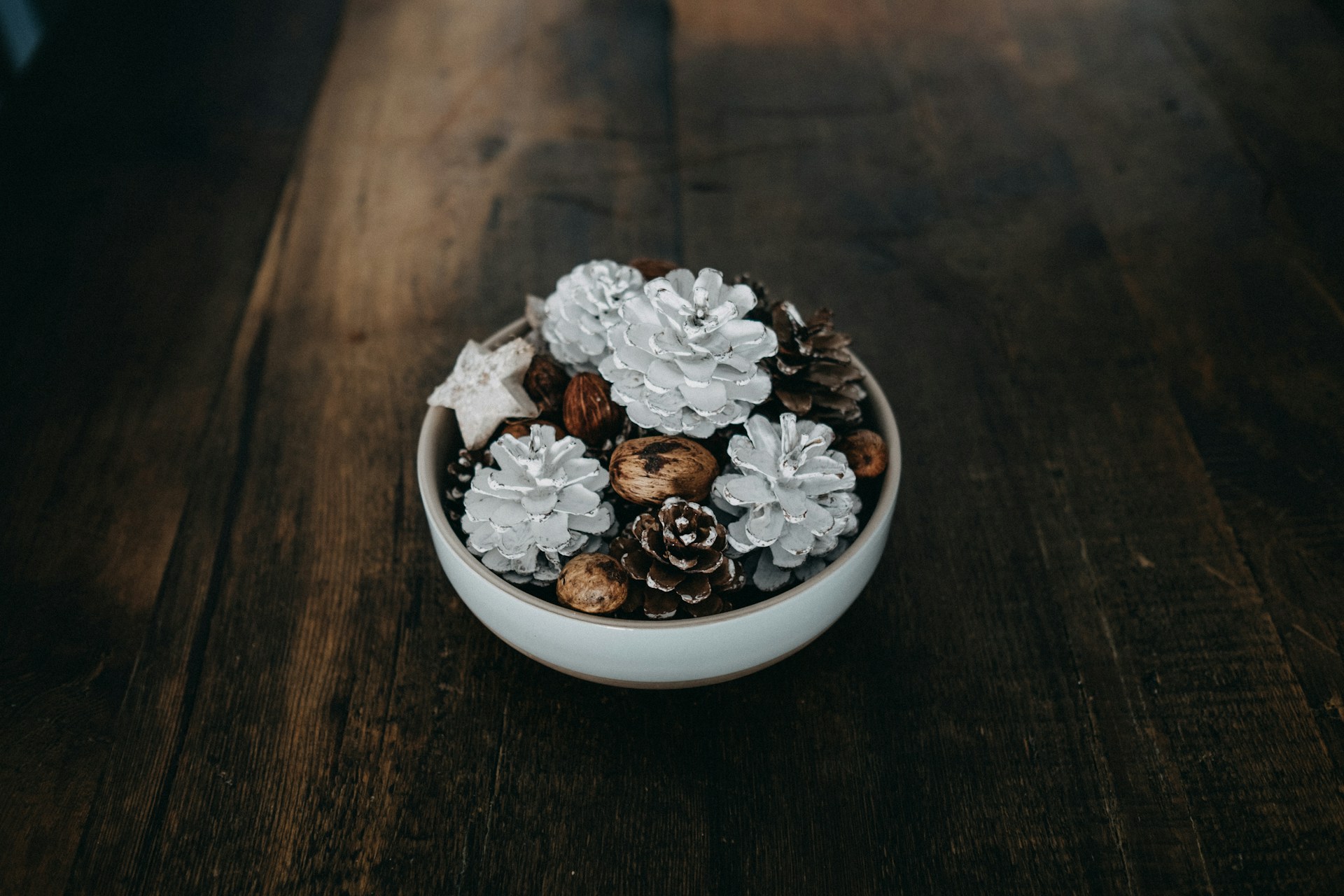 White painted pine cones, natural pine cones and walnuts in a bowl on a dark wooden table