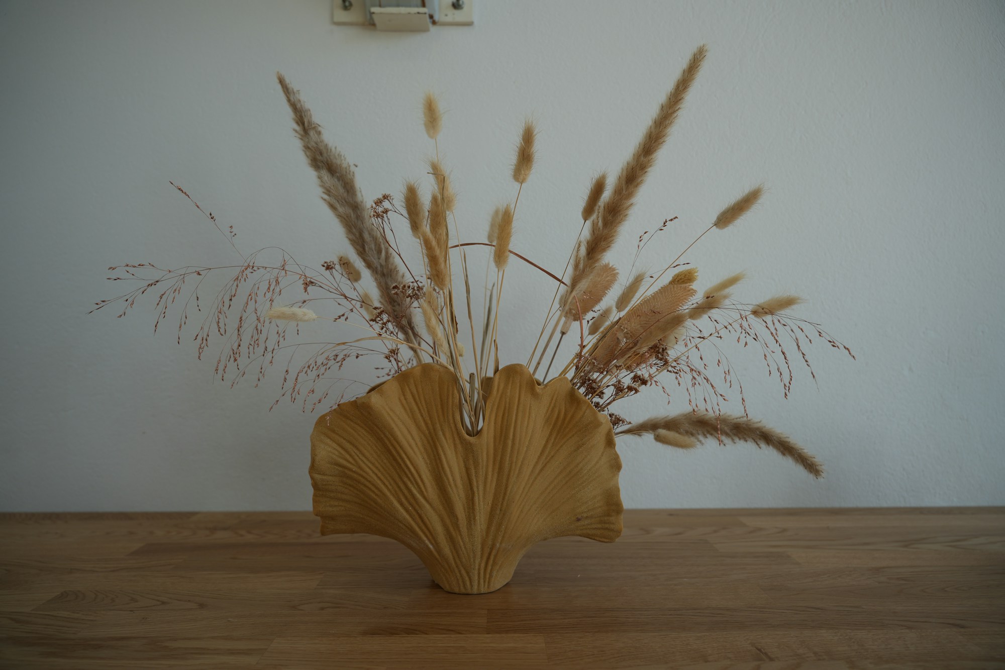 Dried grasses fanned out in a shell shaped vase on a wooden table