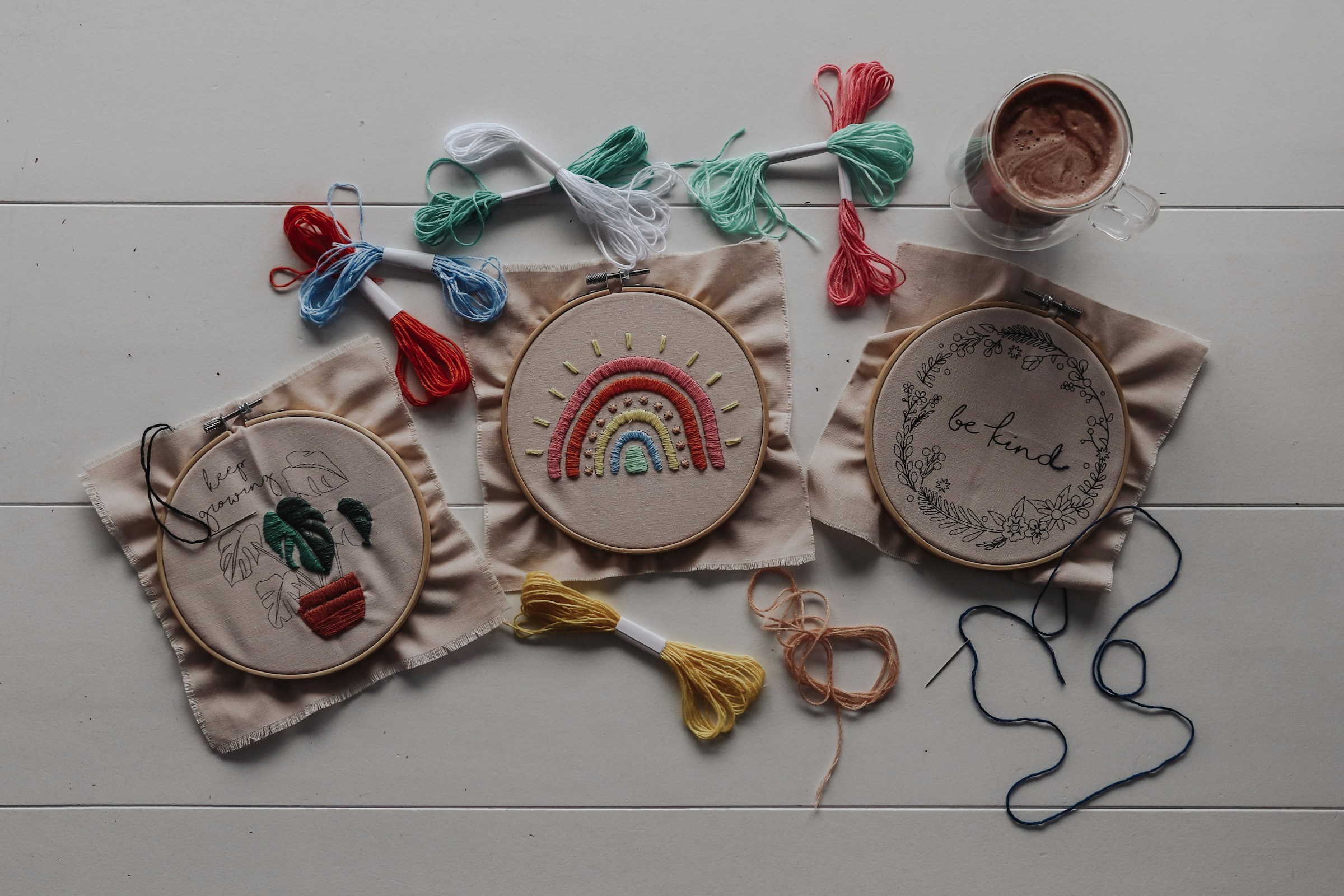Three embroidery hoops with fabric and colorful thread on a table