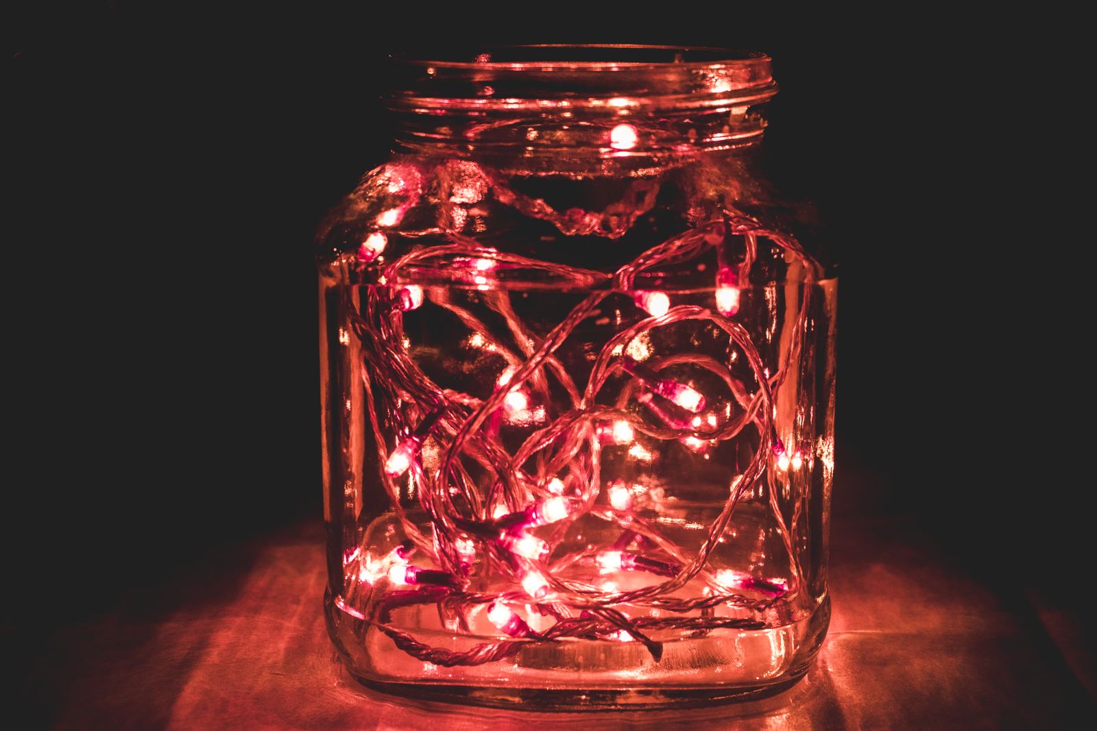 A glass jar filled with glowing red LED fairy lights in a dark room