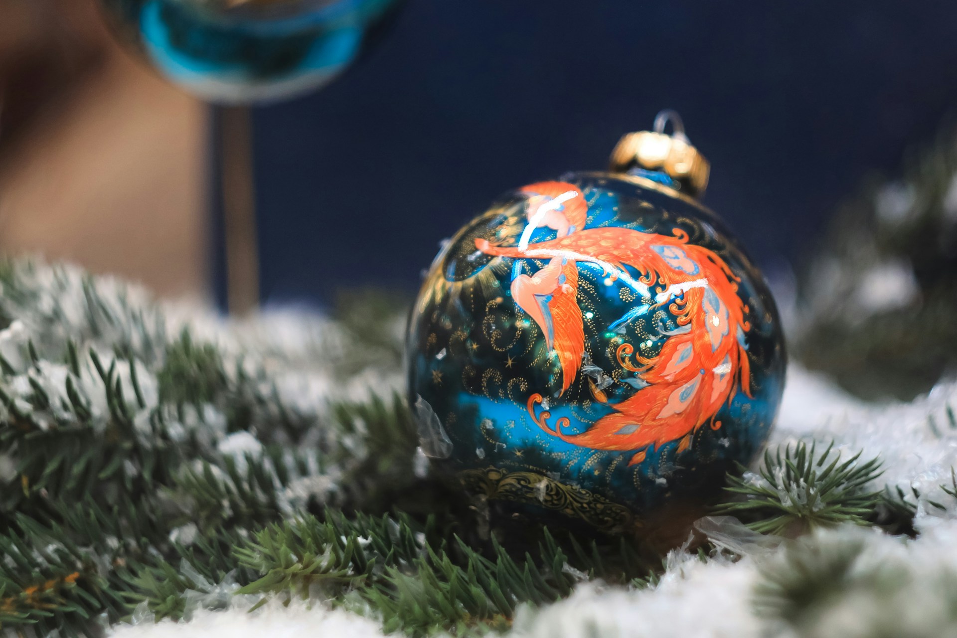 Teal glass ball with an orange folk art firebird and gold swirls