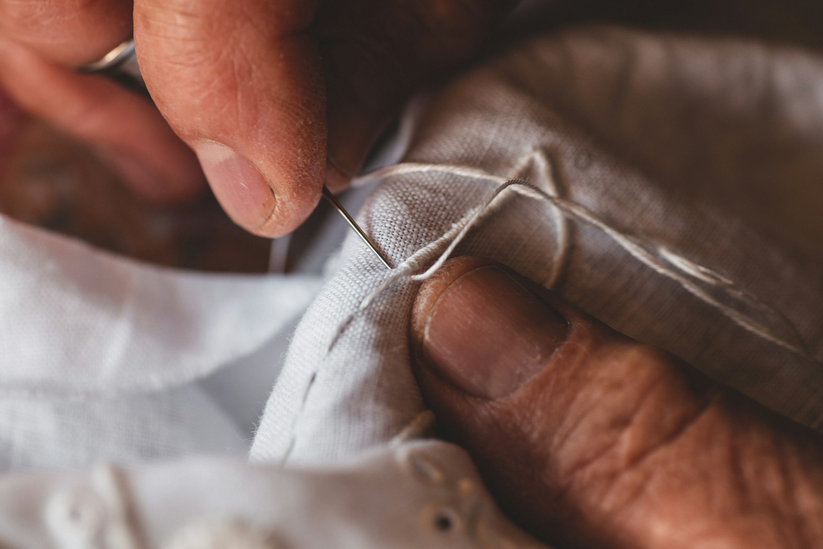 Hands sewing a seam in white fabric with a needle and thread