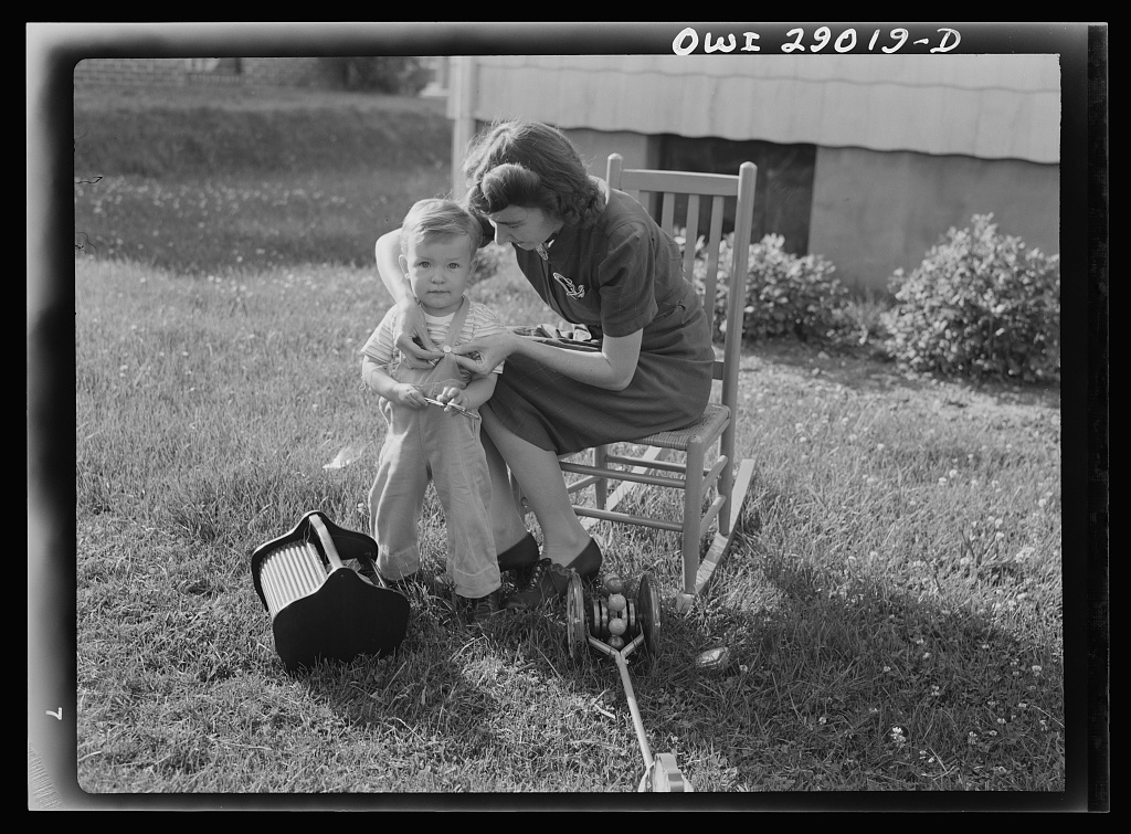 Vintage photo of a mother sewing a button onto her child's overalls