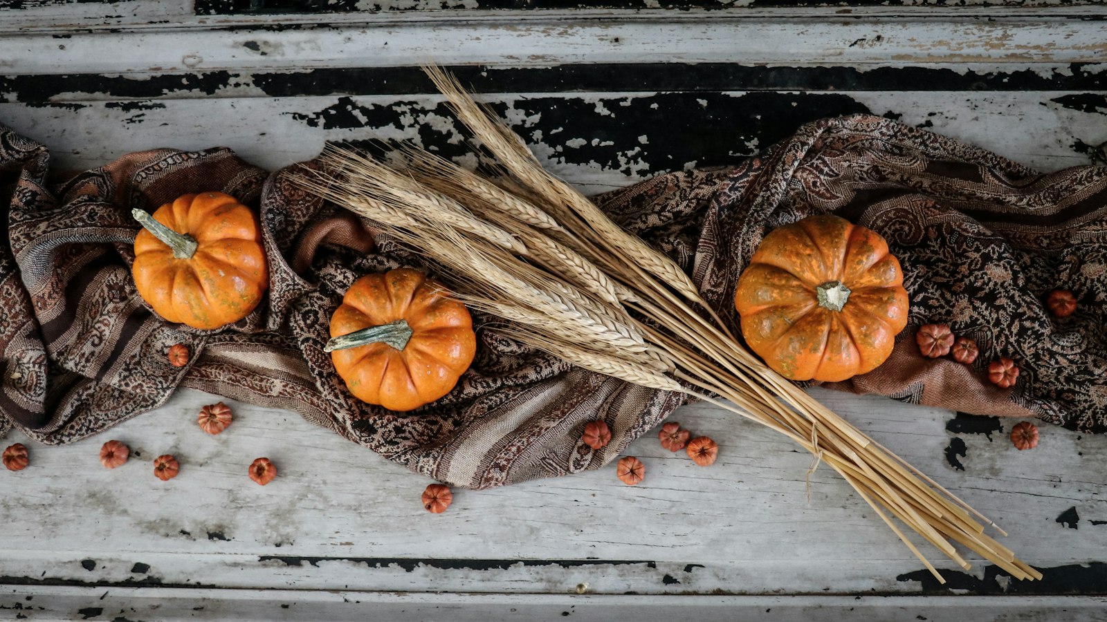 Small orange pumpkins with a bundle of dried wheat on a rustic wooden board