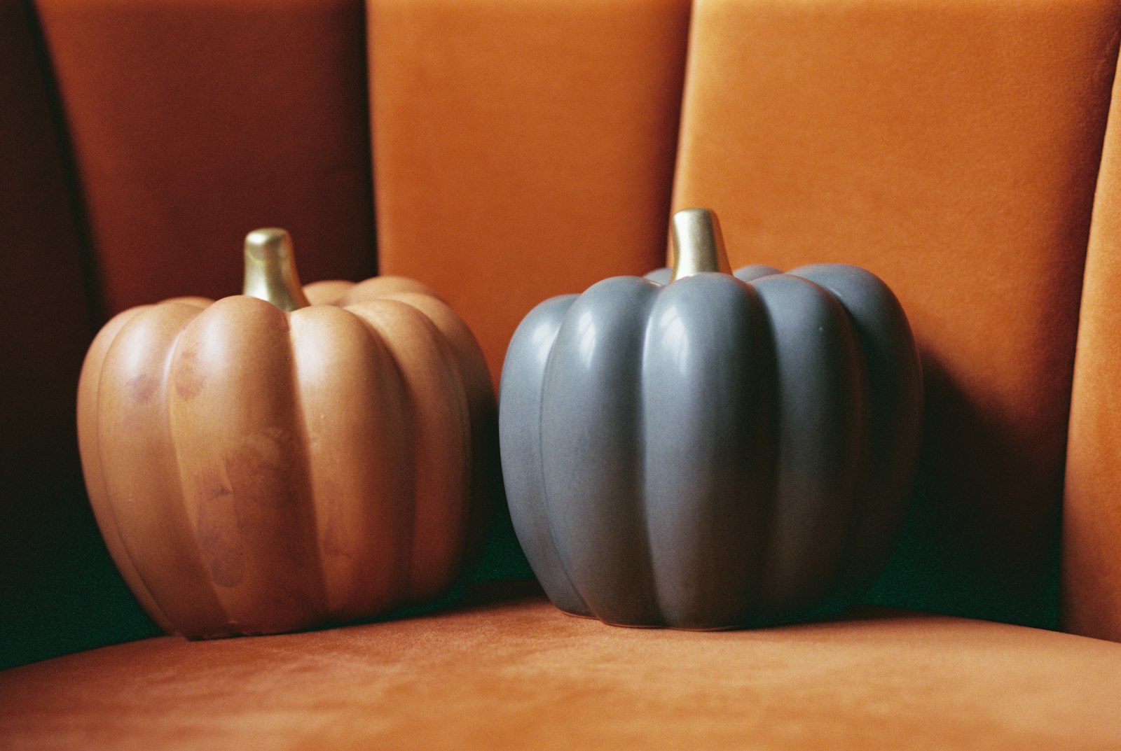A terracotta colored pumpkin and a slate gray pumpkin on an orange velvet chair