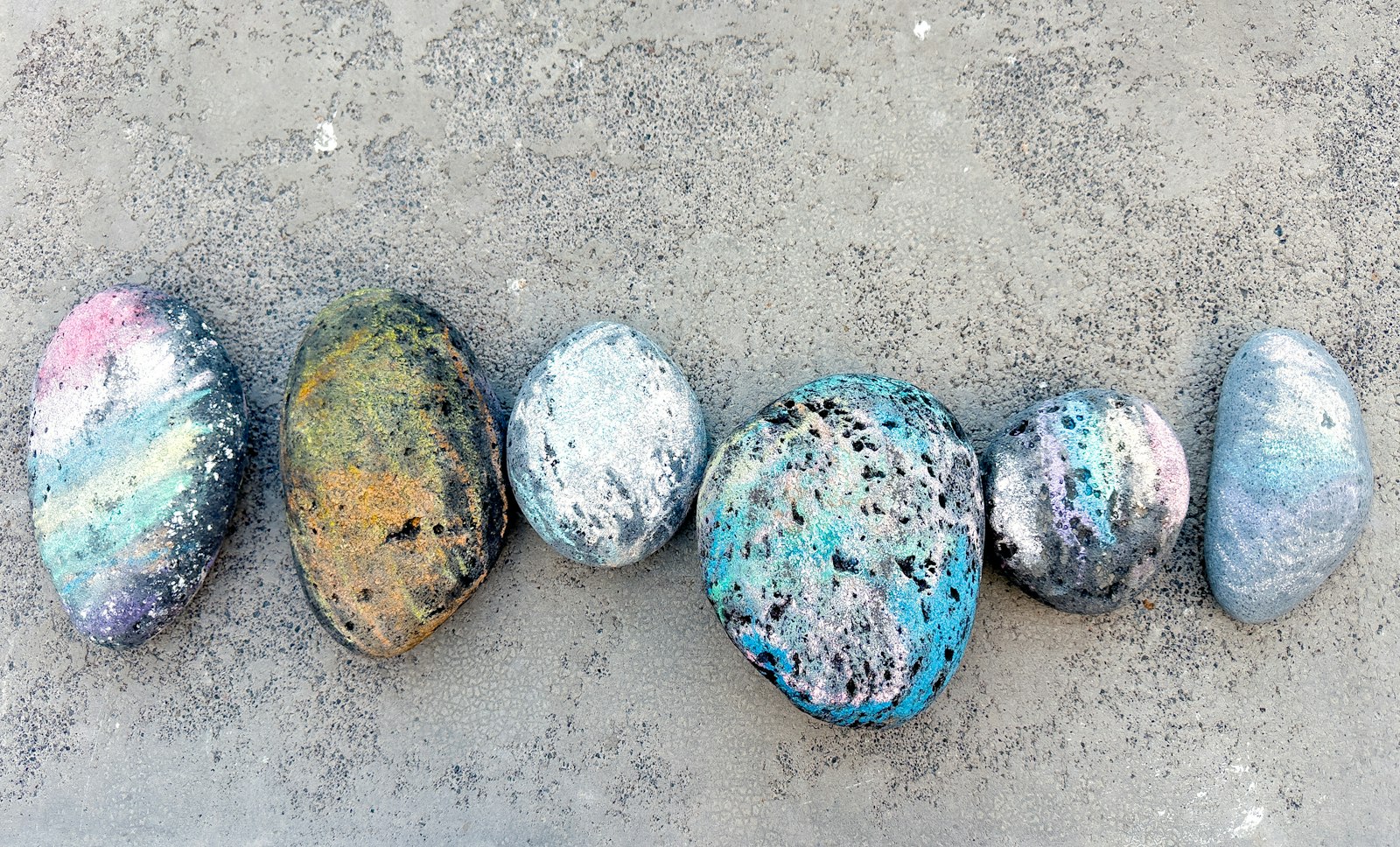 Six colorful hand painted rocks lined up on a gray stone surface