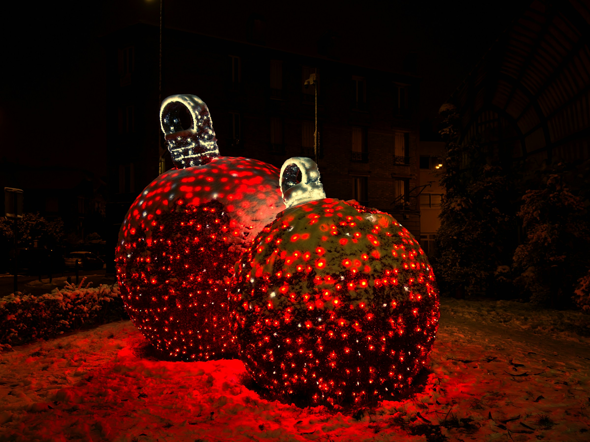 Two giant Christmas ornaments covered in tiny red lights glowing outdoors at night