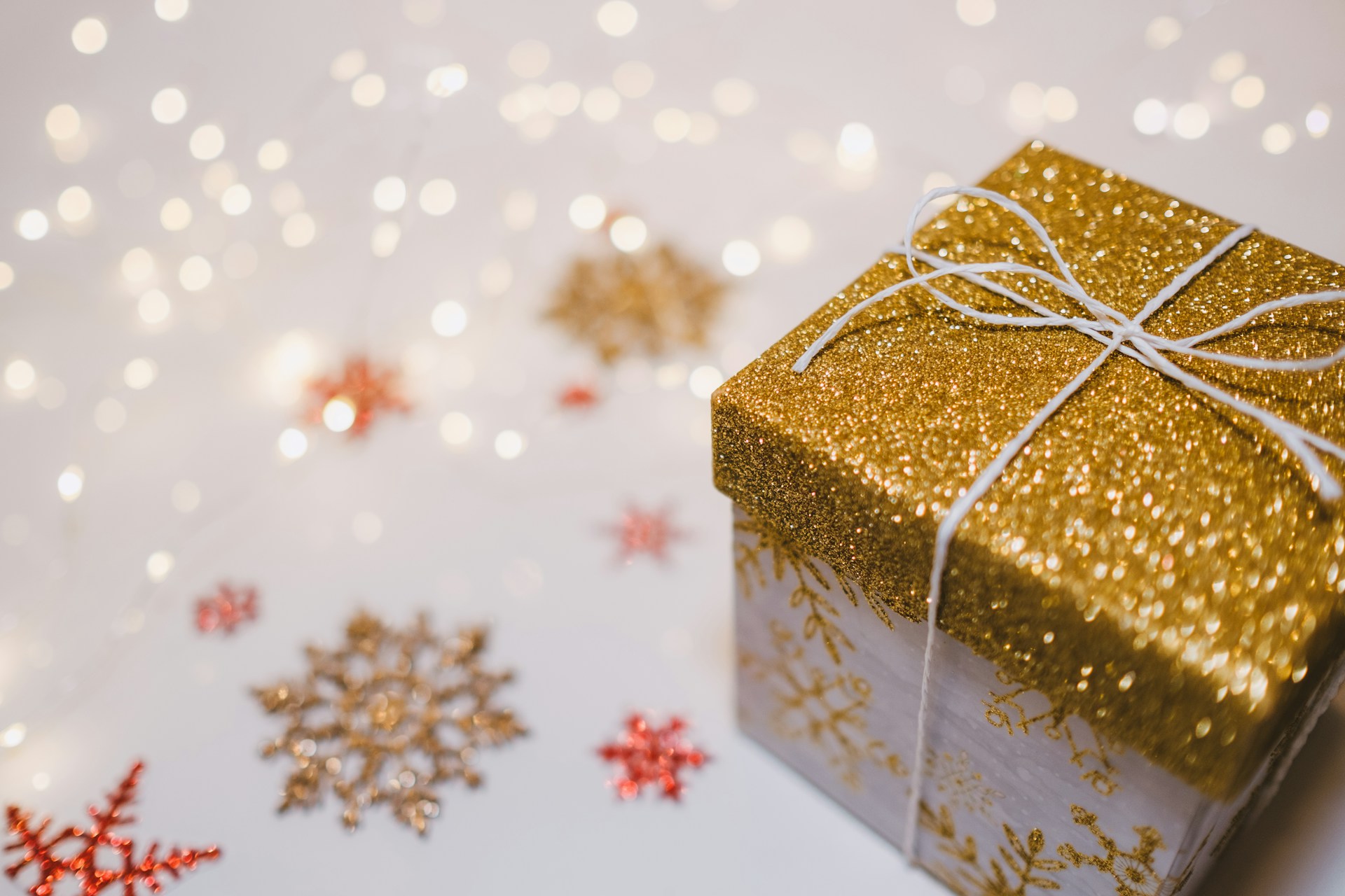 Small gift box with a gold glitter lid tied with silver twine beside paper snowflakes