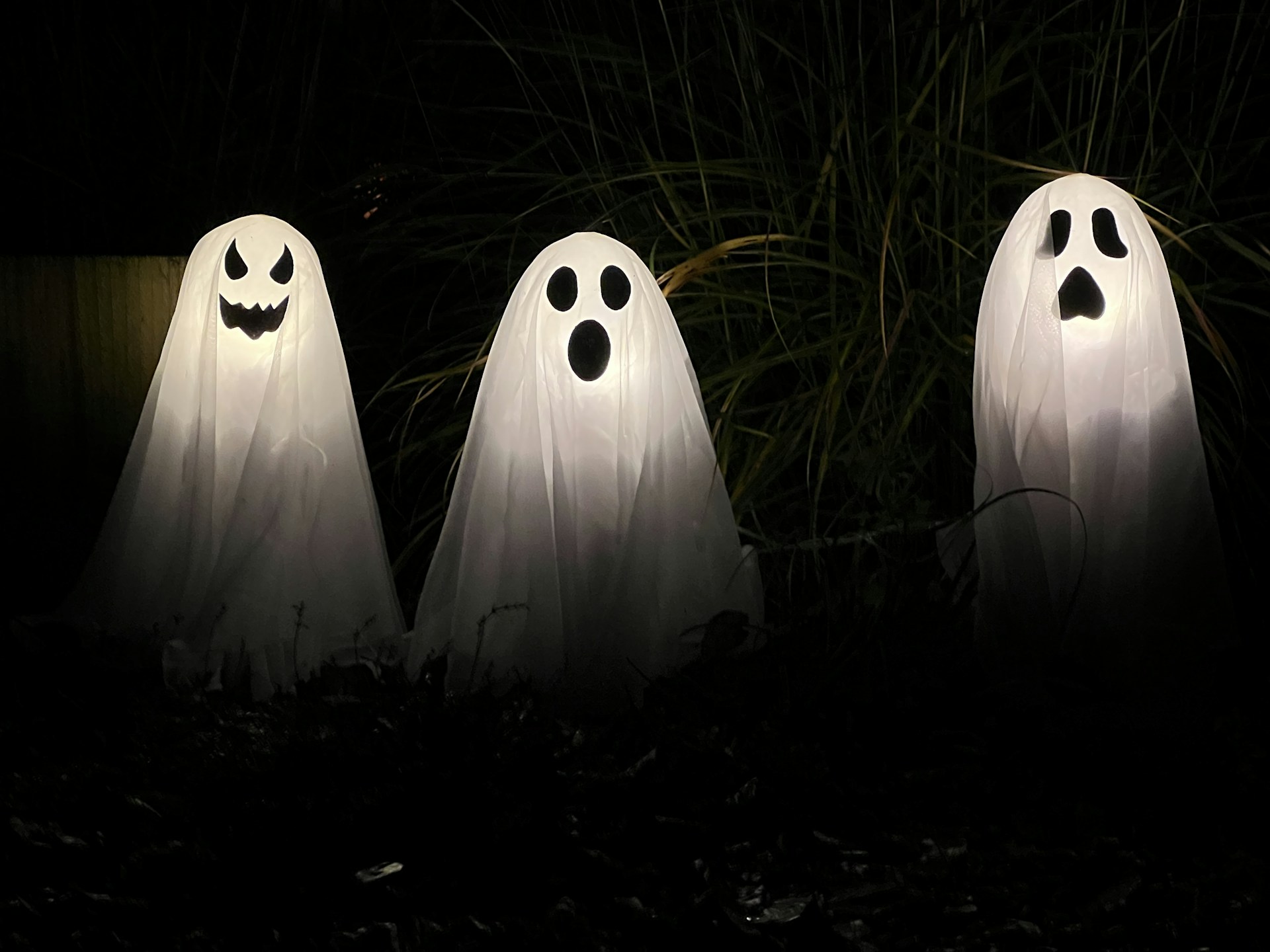 Three glowing white ghost decorations with carved faces in a dark garden