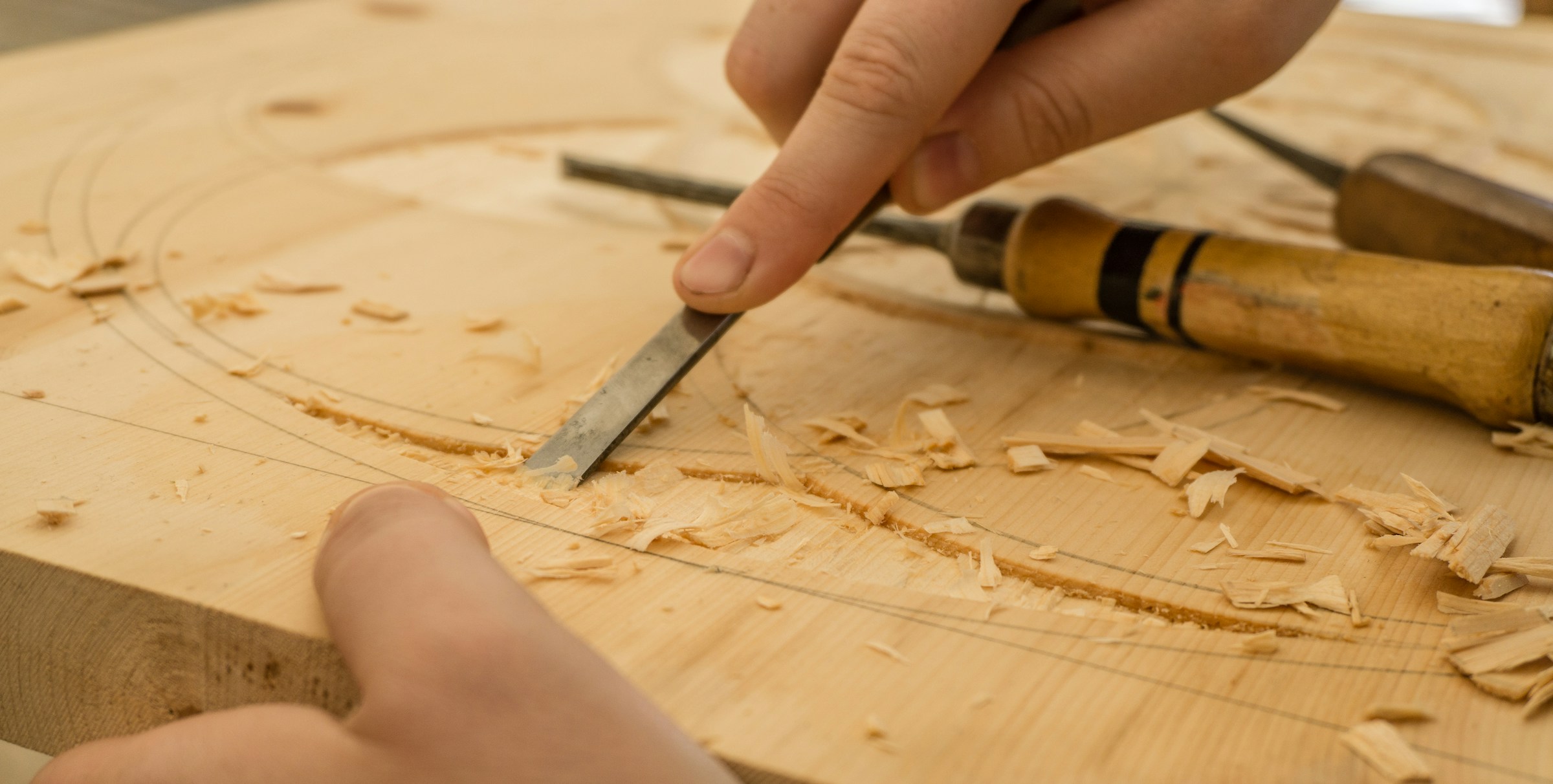 Hands using a chisel to carve texture into a block of wood