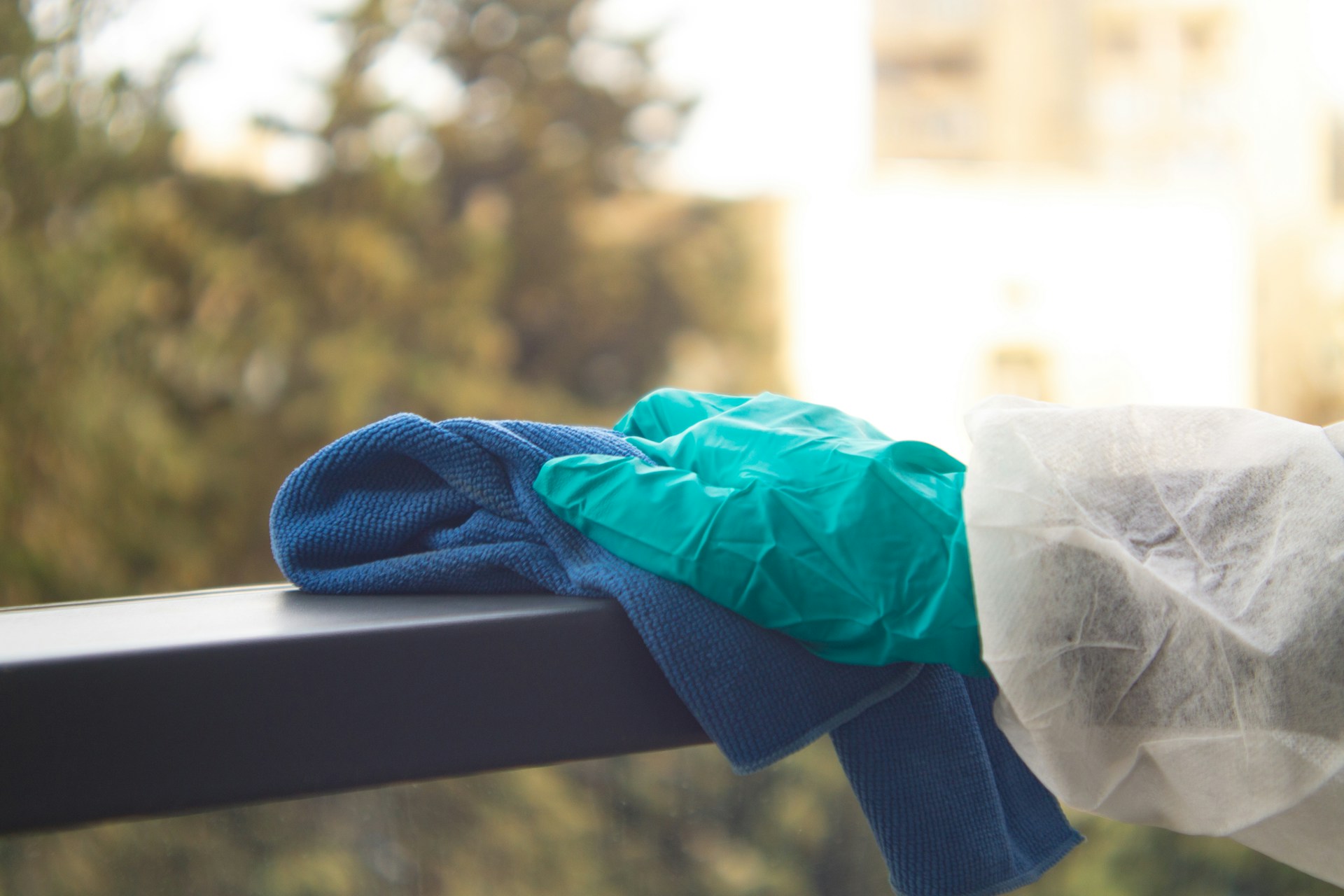 Gloved hand wiping a window frame with a blue cloth