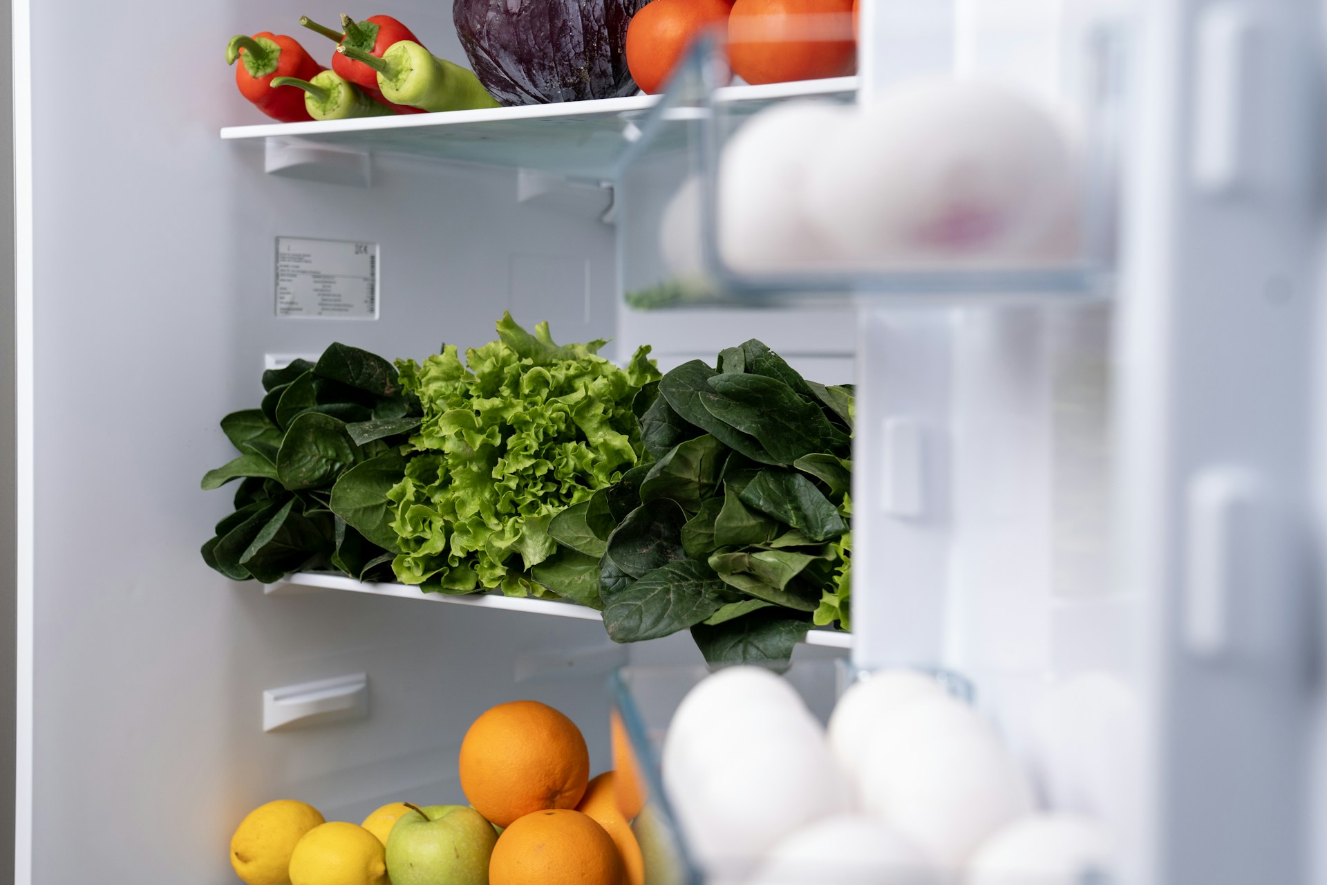 Open refrigerator with greens, eggs and oranges