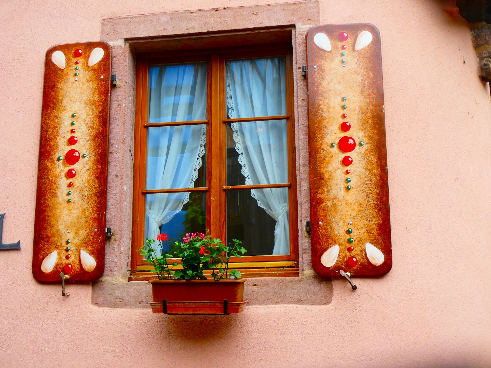 Hand painted decorative shutters beside a window with a flower box