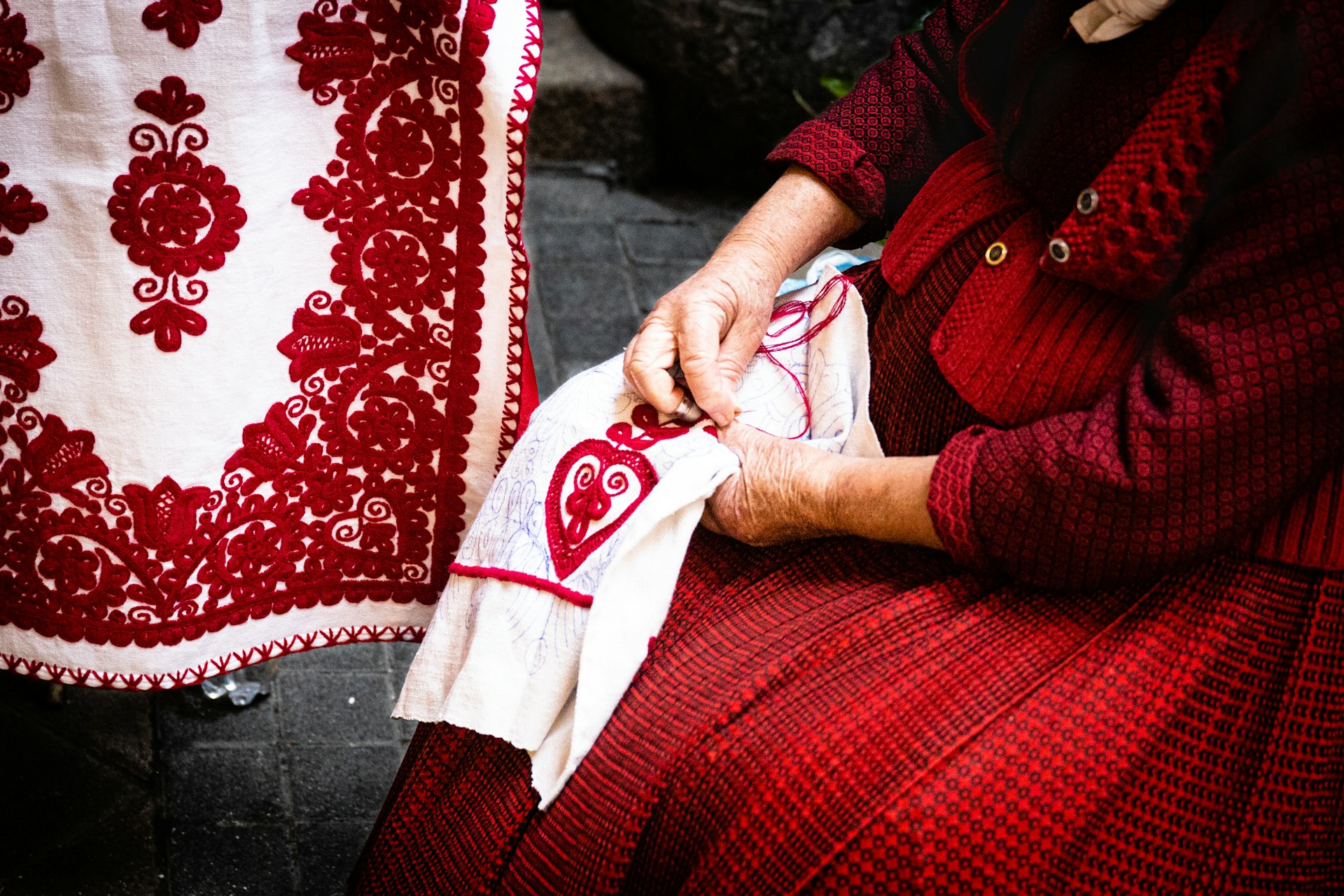Hands stitching red embroidery on white fabric