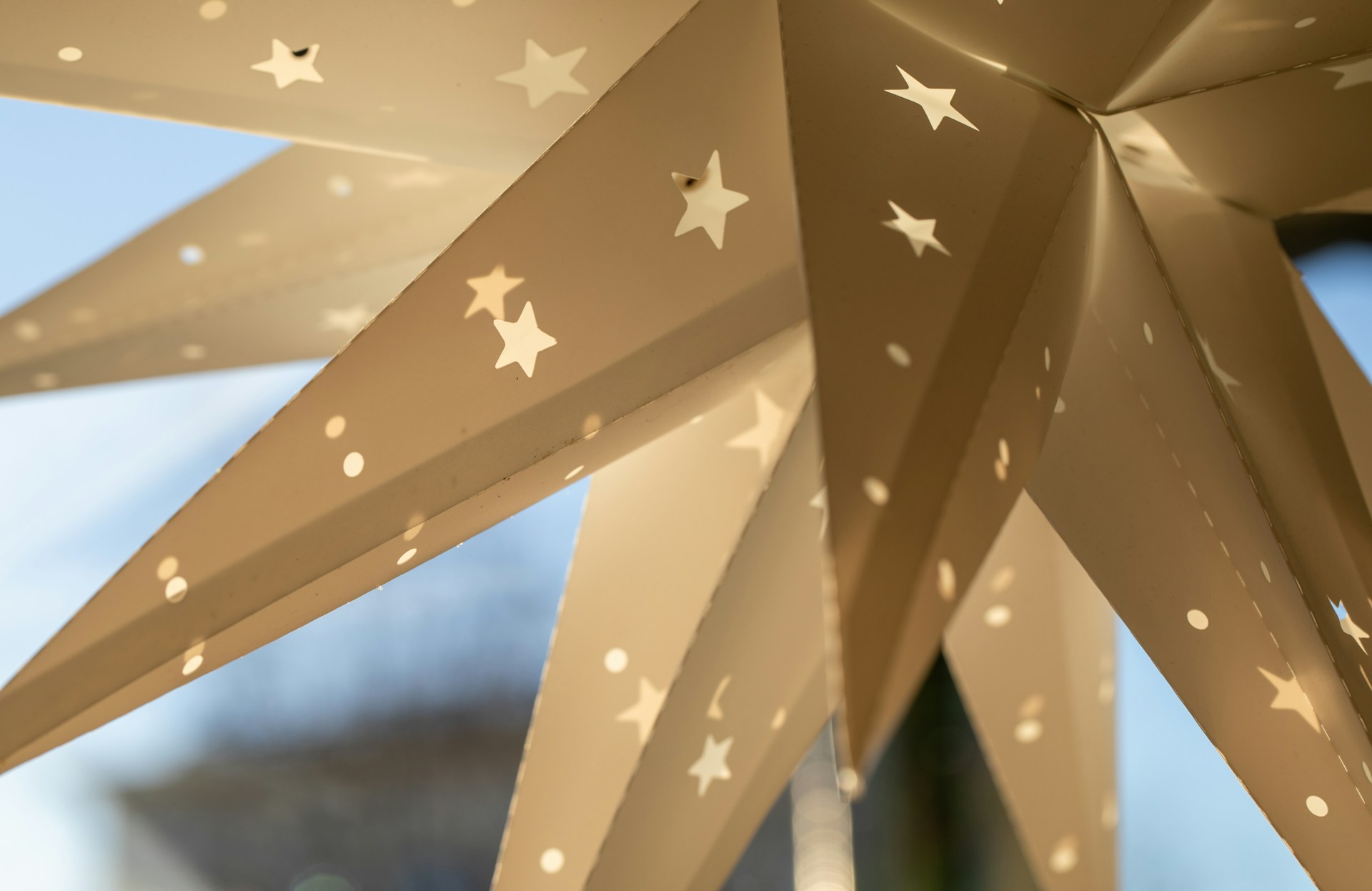 Gold paper star lantern with tiny star cutouts hanging in a window