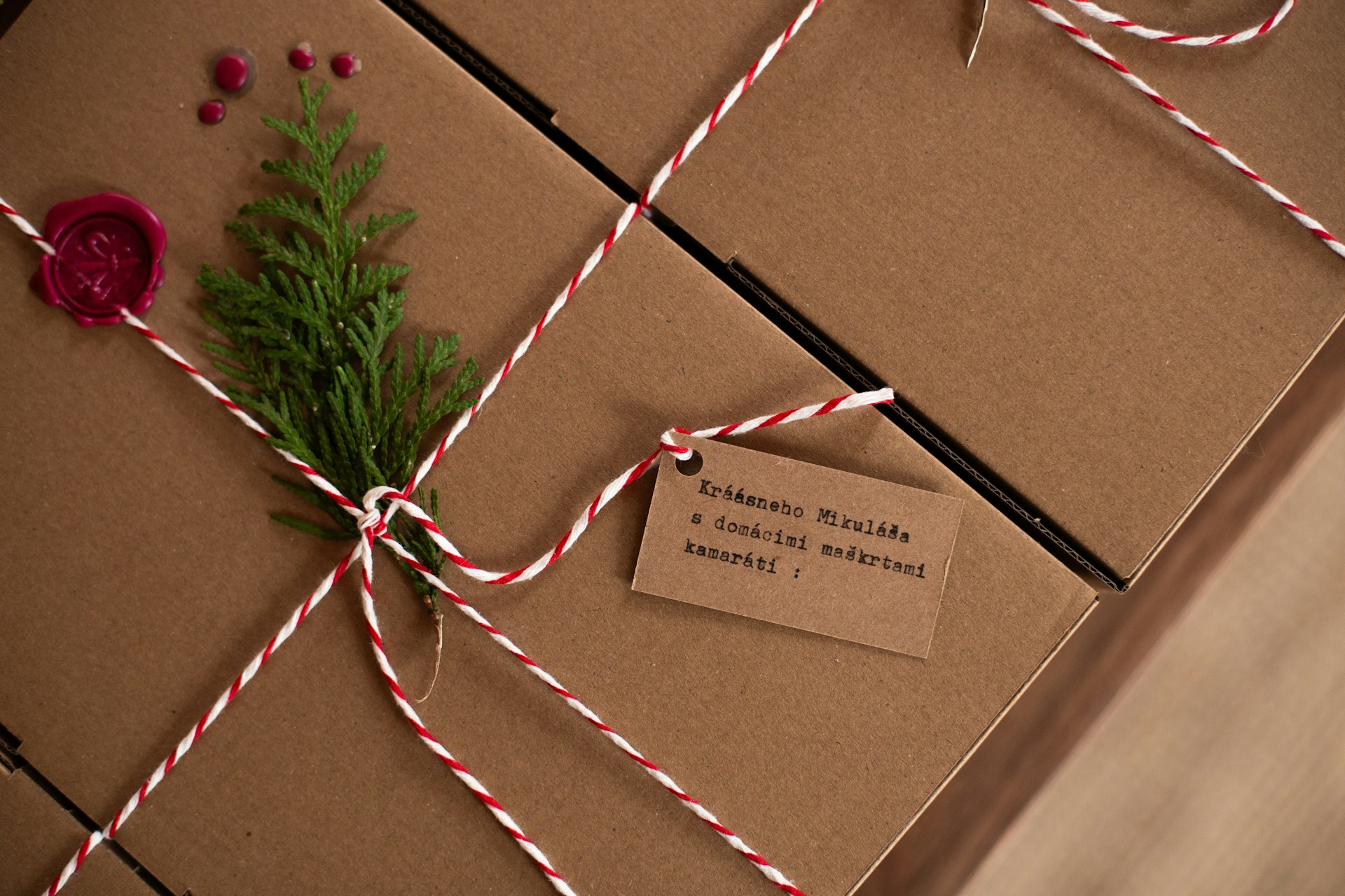 Kraft paper gift boxes tied with red and white twine and a sprig of greenery