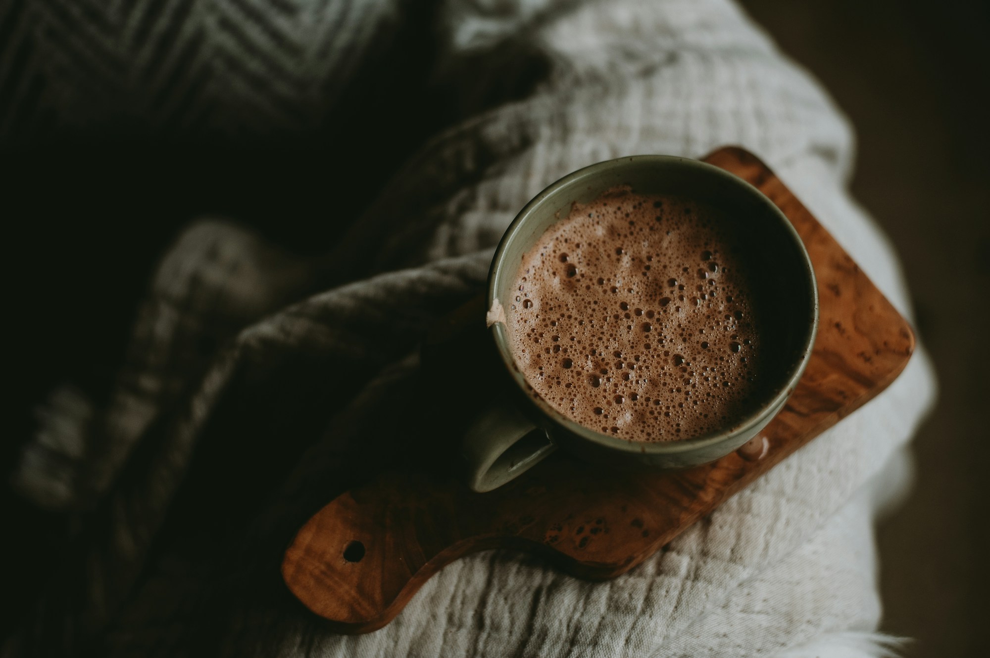 A mug of hot cocoa on a wooden board with a cozy knit blanket
