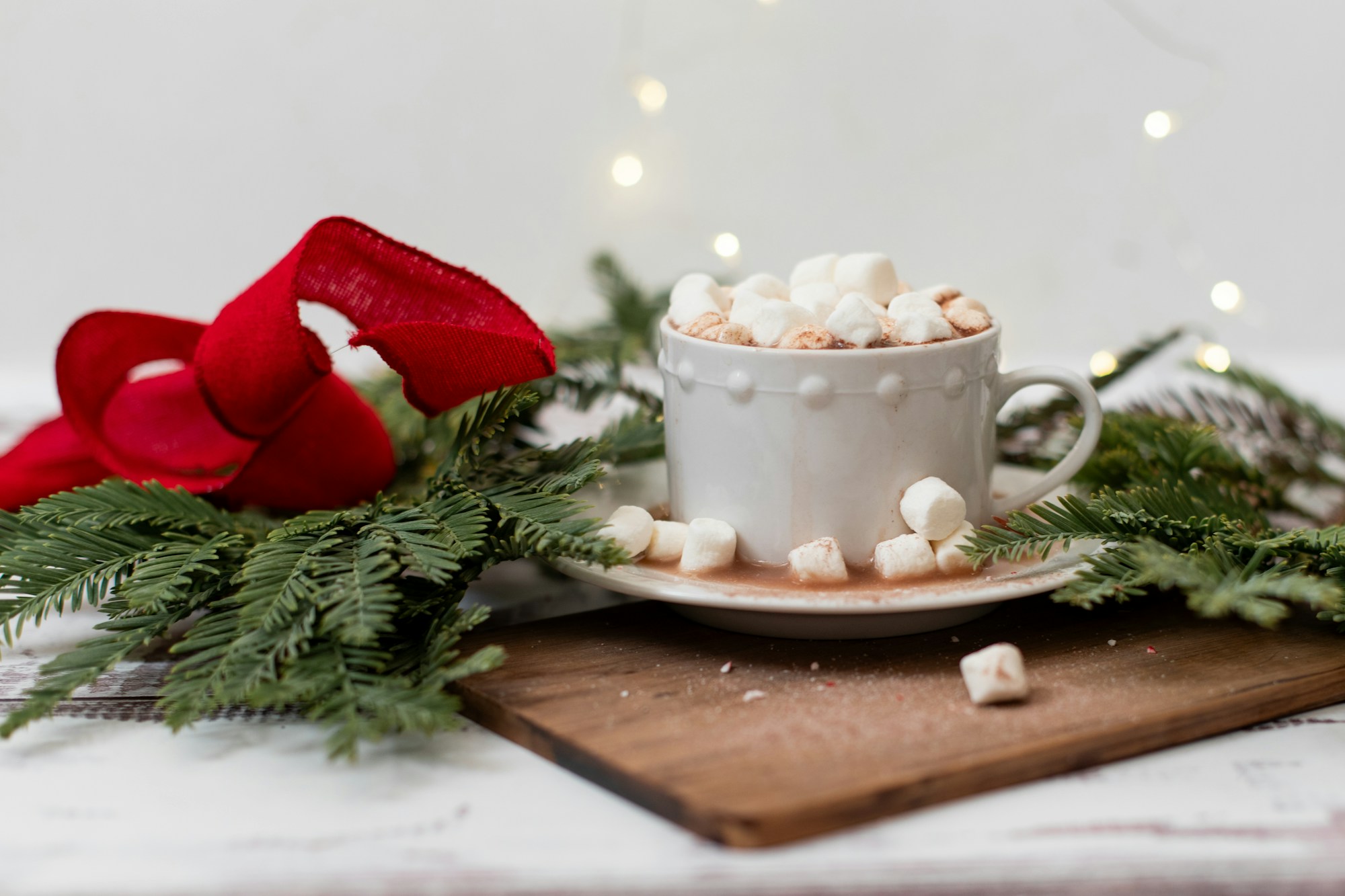 Hot cocoa bar ideas: a mug of cocoa topped with marshmallows beside greenery and a red velvet bow