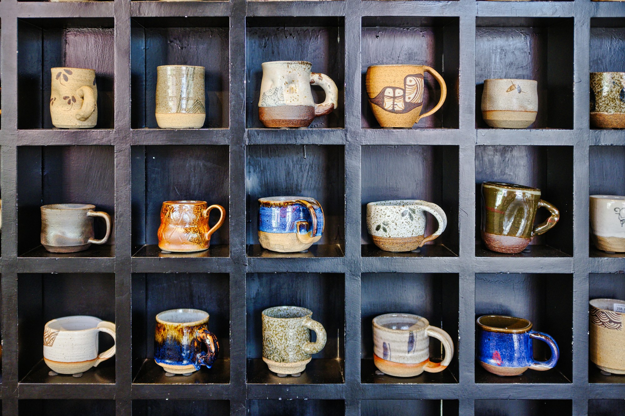 Handmade mugs displayed in a dark wooden cubby shelf