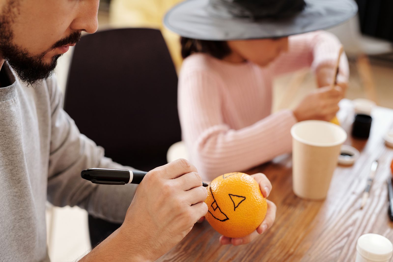 Parent and child drawing a jack-o-lantern face on an orange with a marker