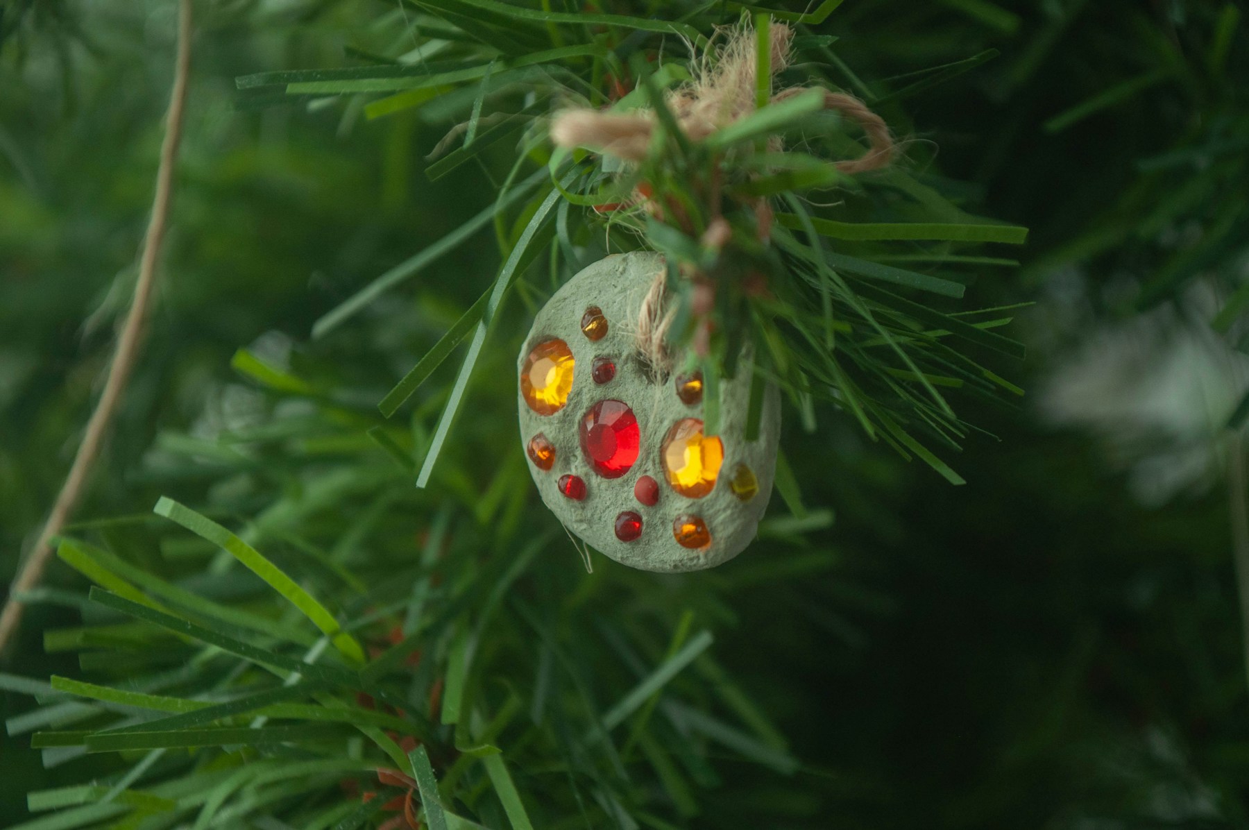 Handmade ornament covered in colorful gems on a Christmas tree, one of the prettiest recycled Christmas decorations