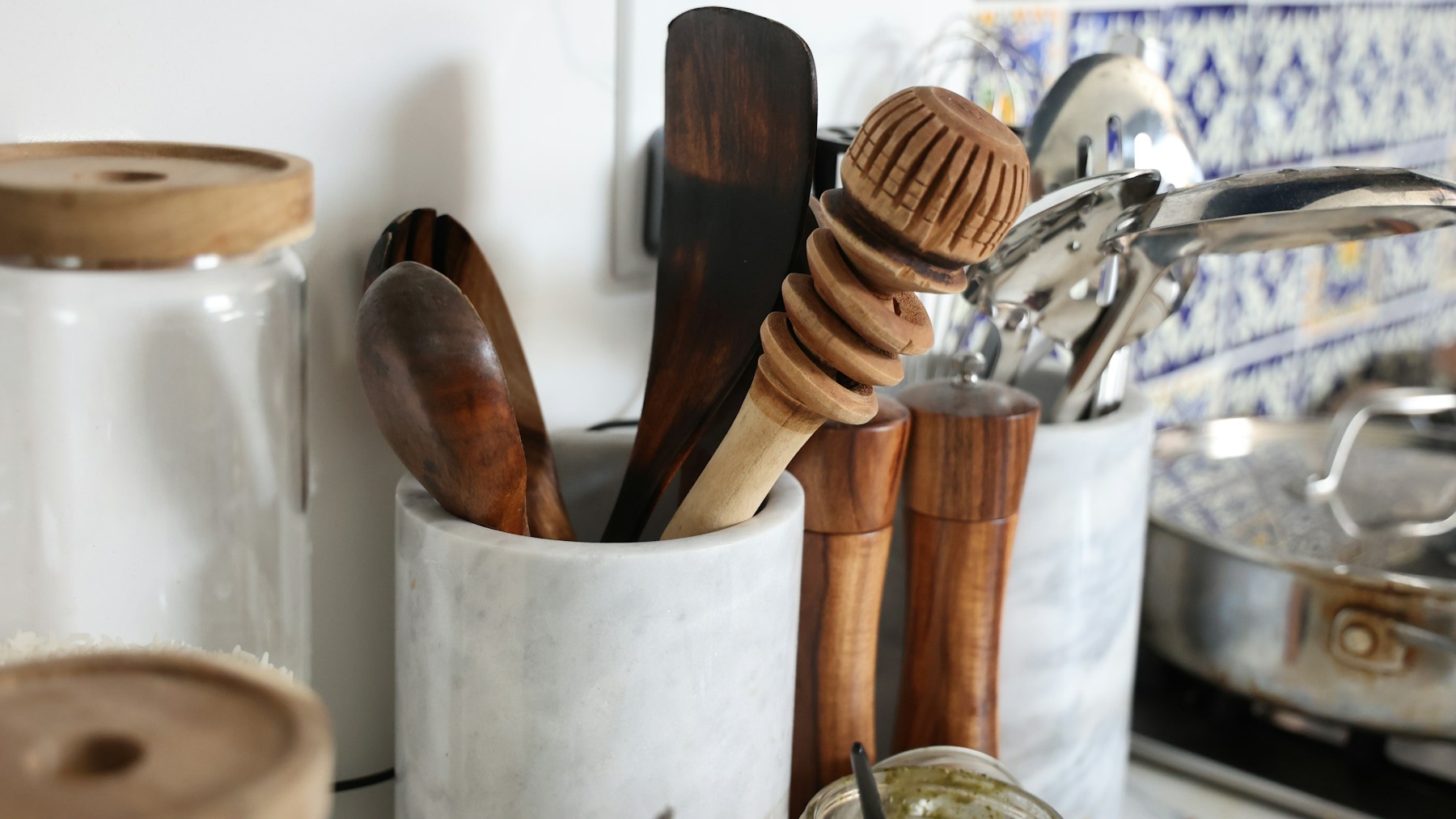 Wooden spoons, a honey dipper and metal ladles in a marble utensil crock beside the stove