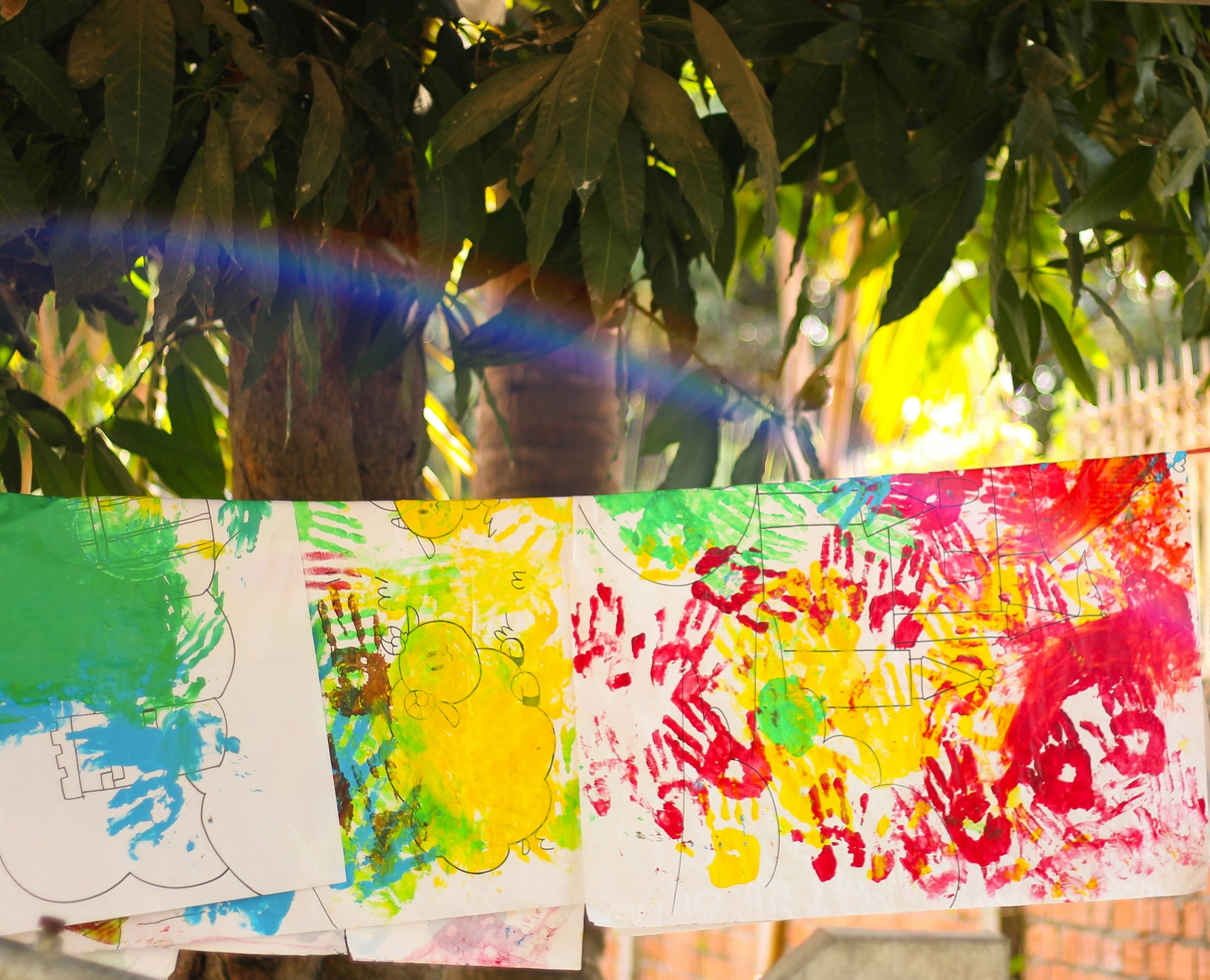 Colorful children's handprint paintings hanging on a line outdoors
