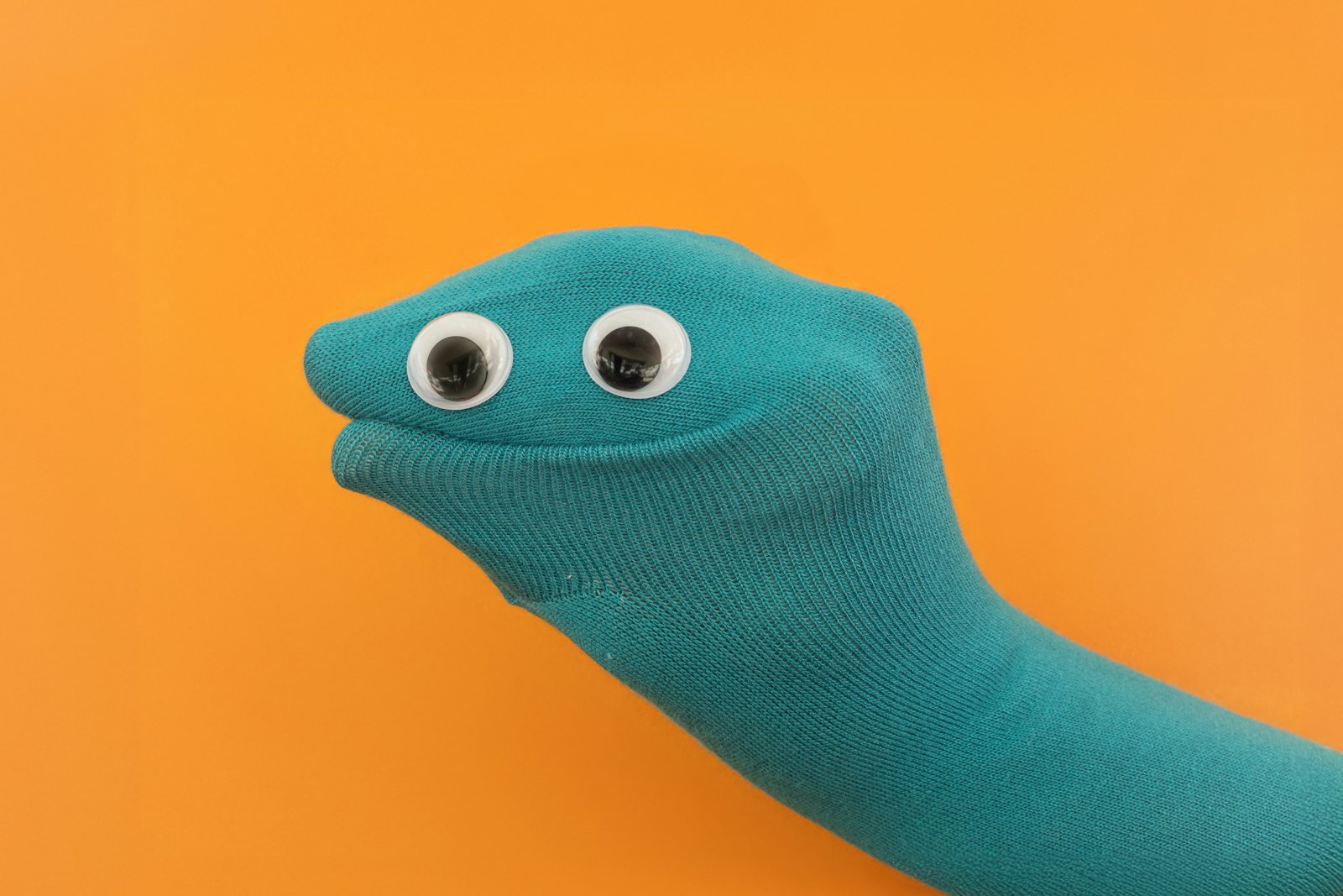 Teal sock puppet with googly eyes on an orange background