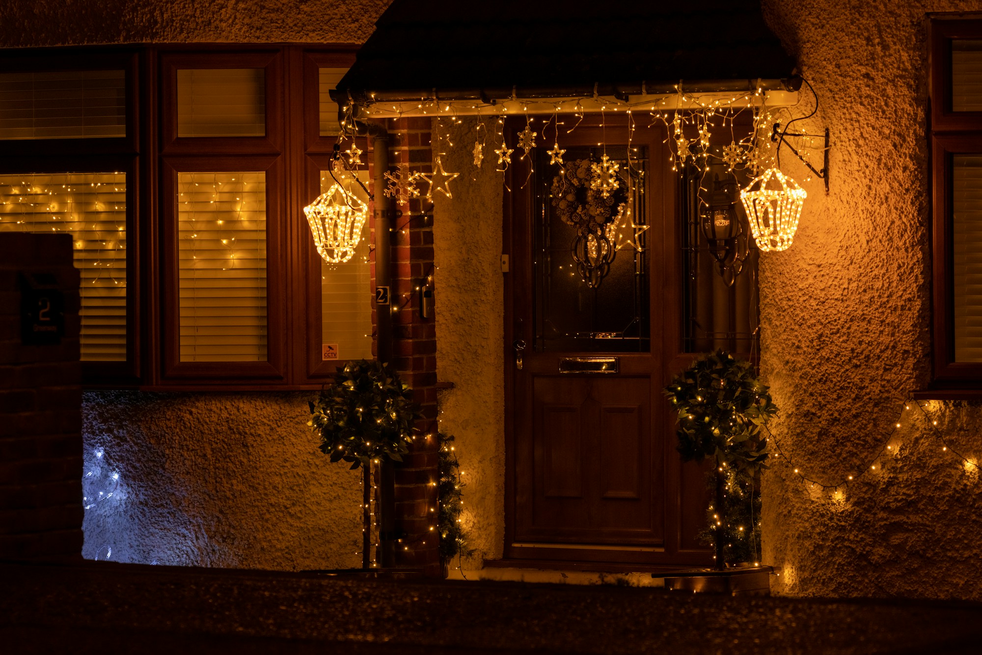 Front door at night framed with warm string lights, lantern lights and greenery