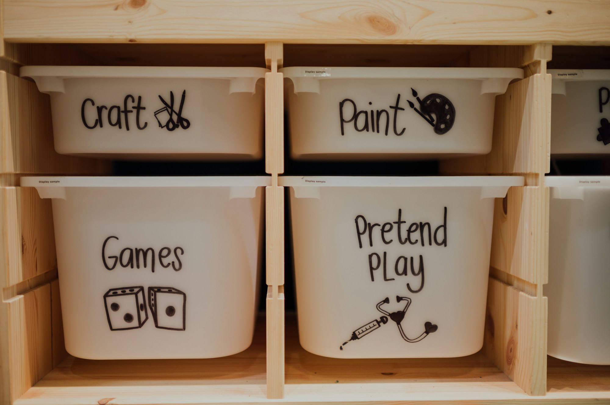 Labeled toy bins for crafts, paint, games and pretend play on a wooden shelf