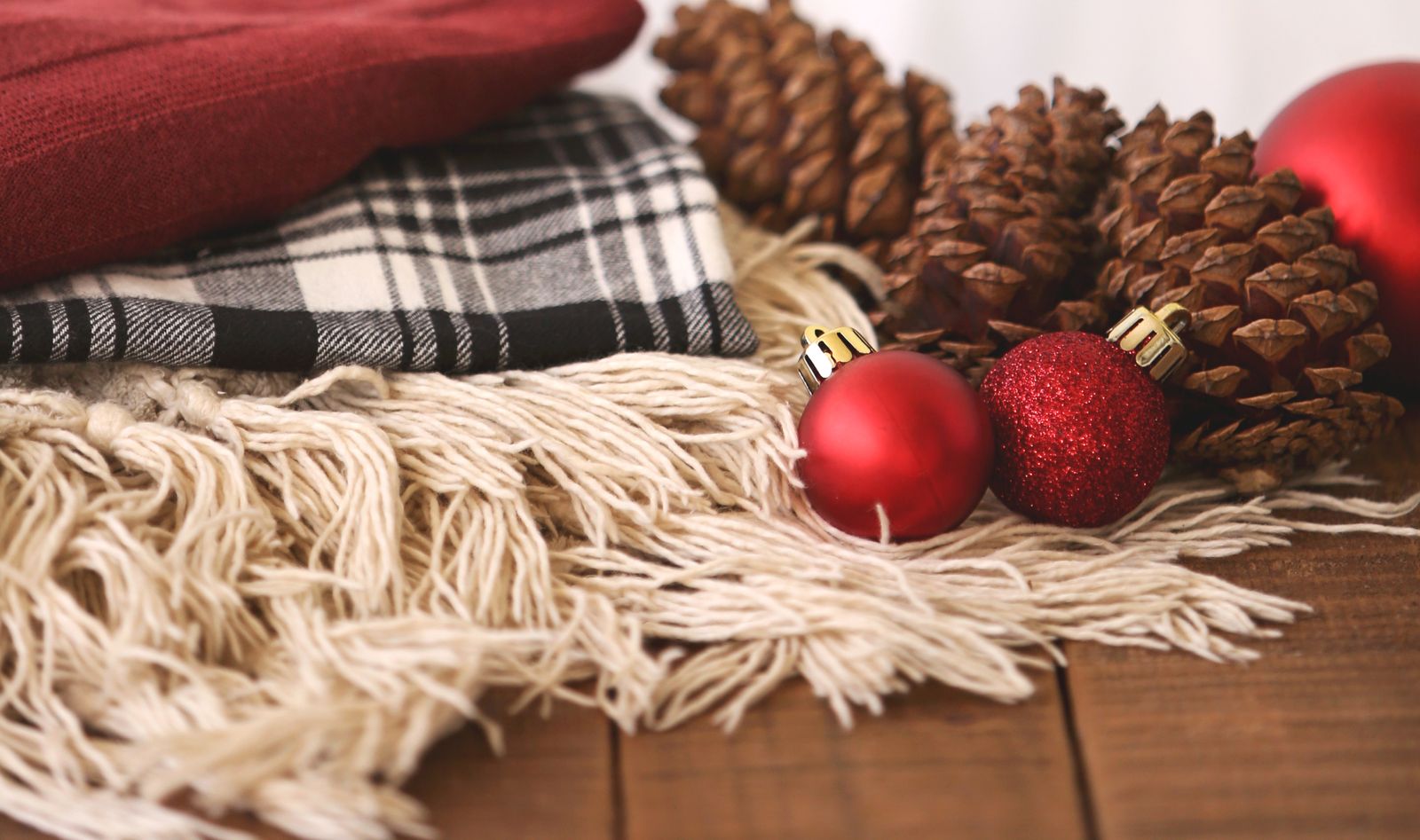 Folded plaid throws with pinecones and red ornaments on a wooden table