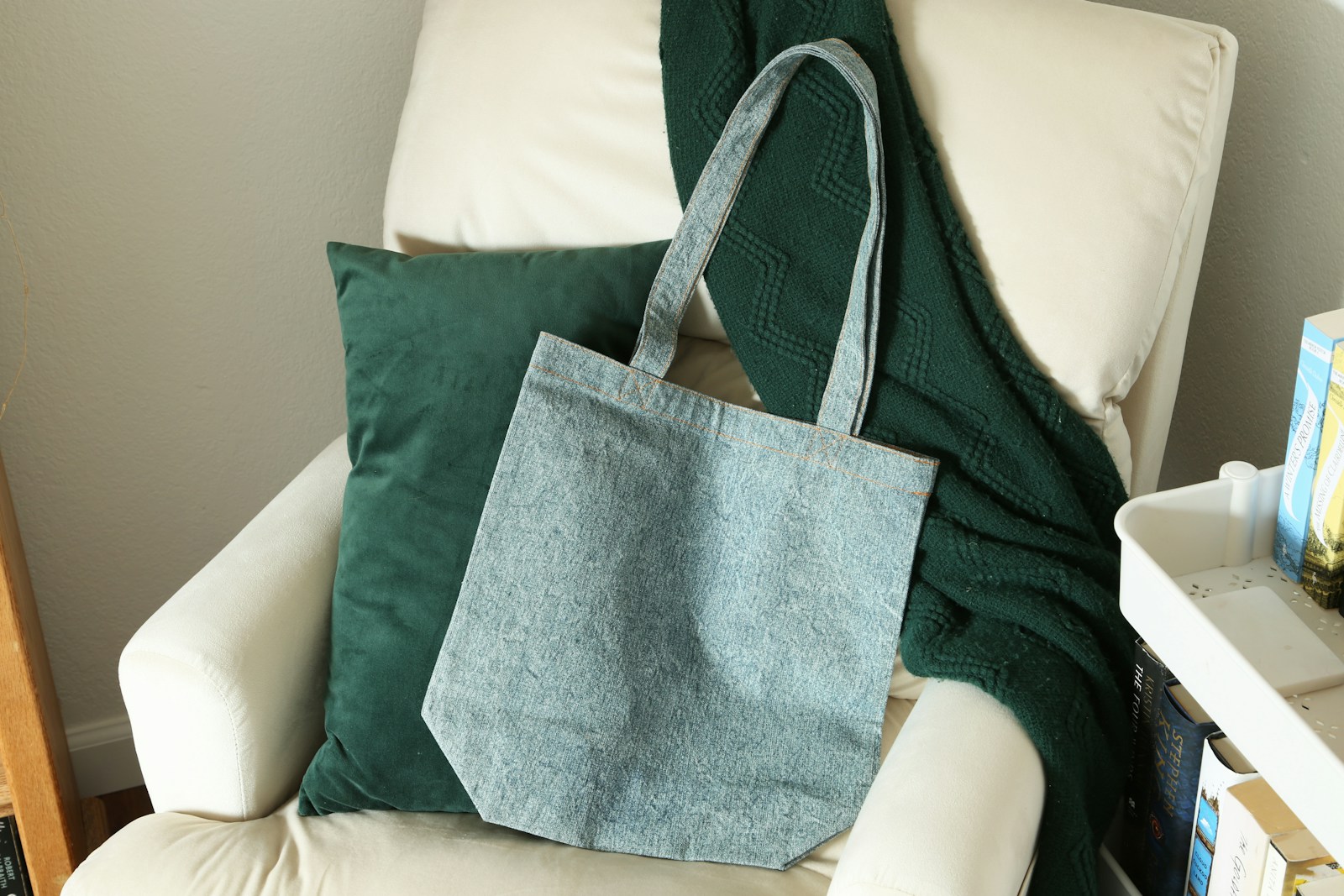 Light blue canvas tote bag on a white armchair with a green pillow and throw