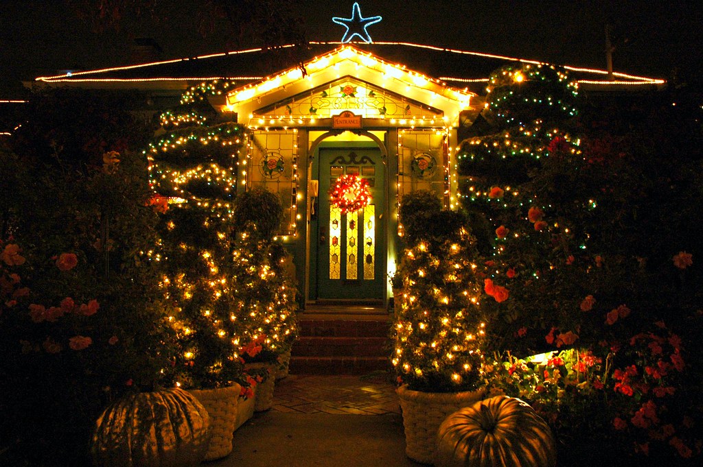 Glowing light wrapped topiary trees framing a front entrance at night