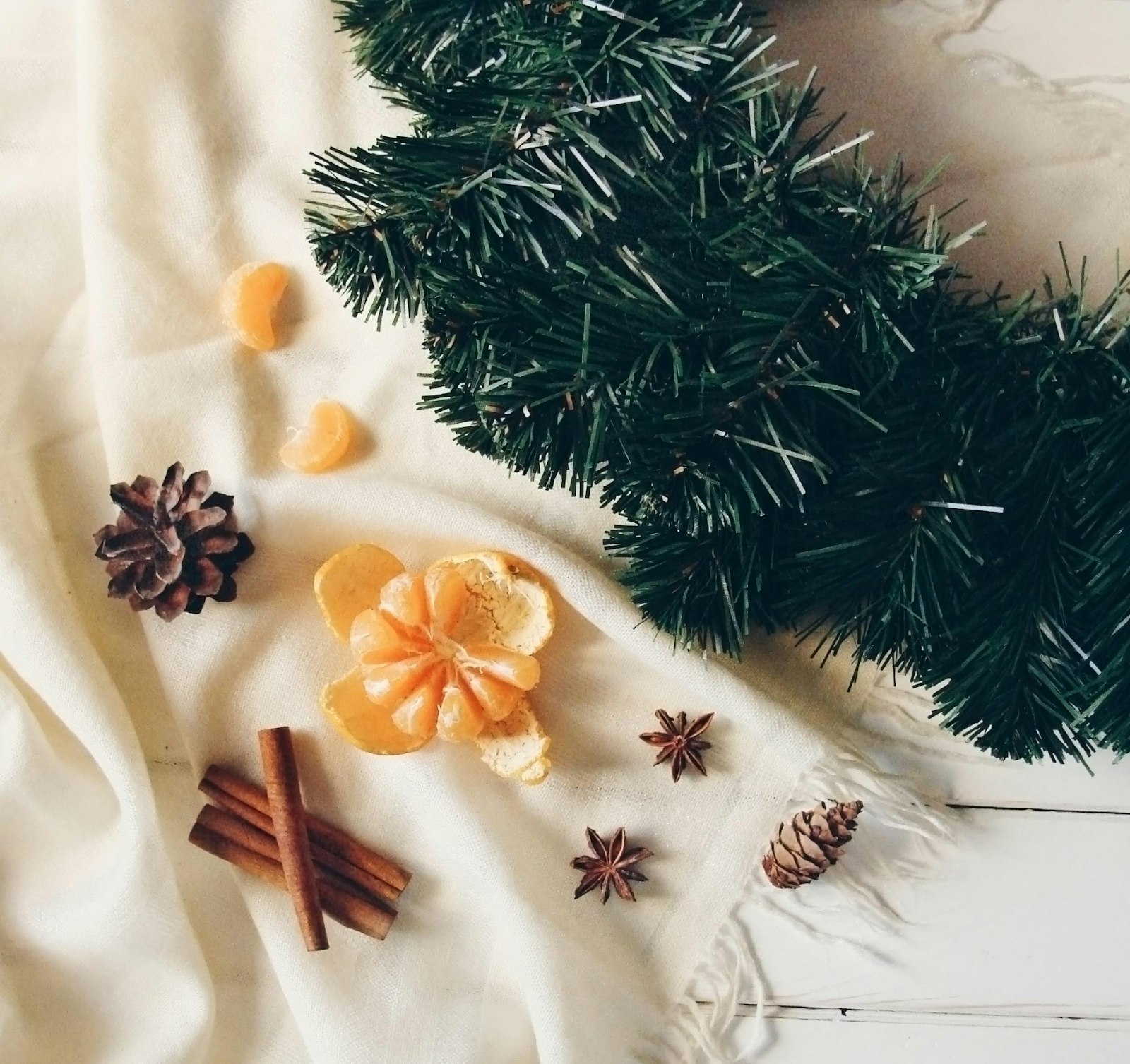 Martha Stewart Farmhouse Christmas table idea with clementines, pine cones, cinnamon and star anise on linen beside greenery