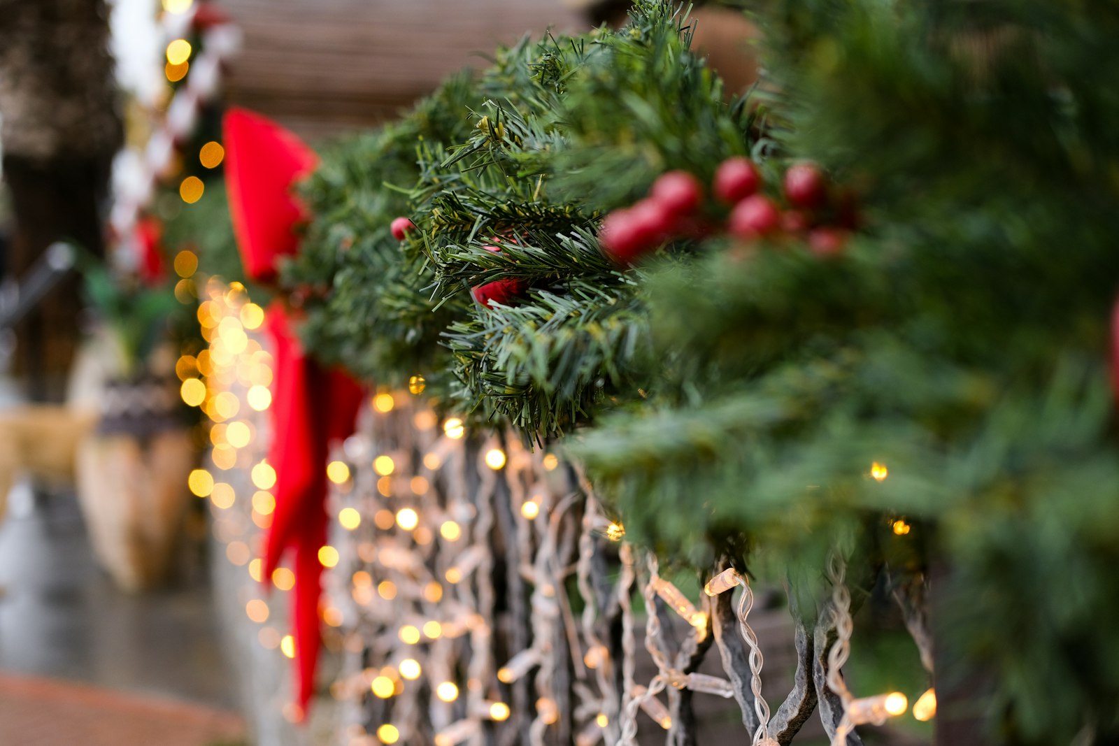 Fresh pine roping with red bows and twinkle lights along a porch rail