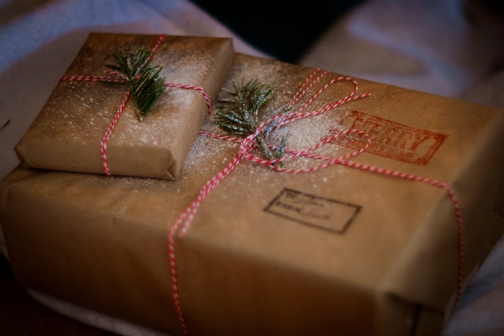 Gifts wrapped in brown kraft paper with stamped greetings, red and white twine and pine sprigs