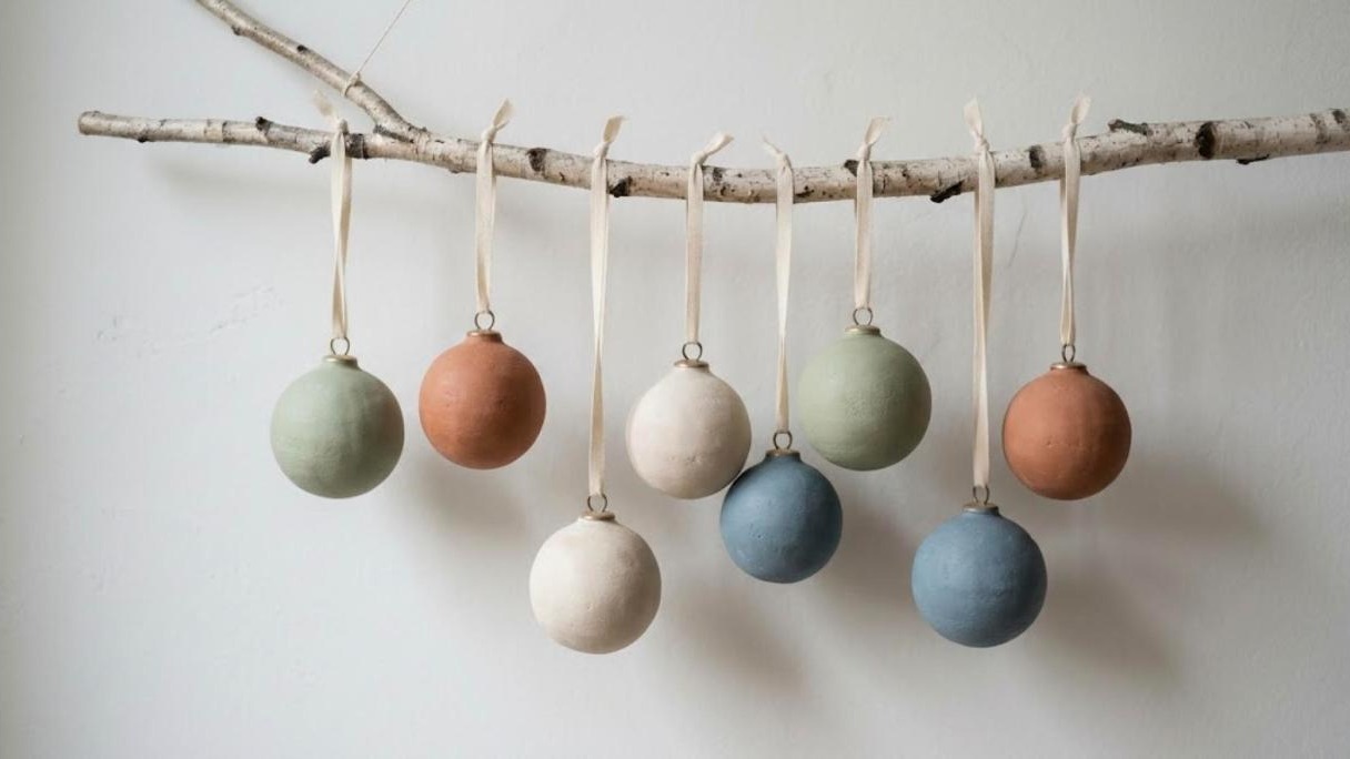 Matte chalk painted ornaments in sage, terracotta, cream and dusty blue hanging from a birch branch